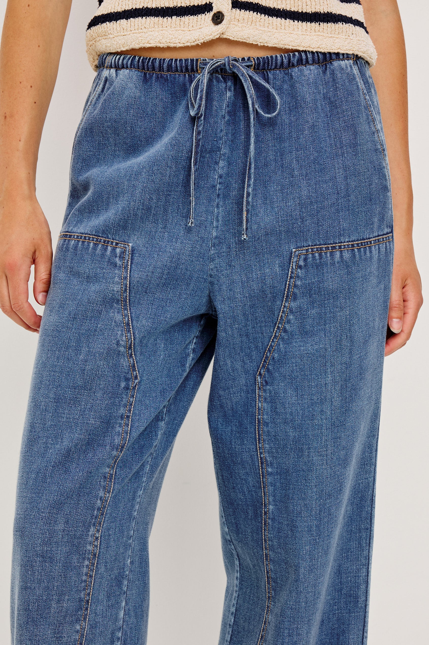 The Sanderson is a wide leg pull on pant with an encased drawstring waist tie, it has workwear inspired contrast topstitching on the front leg panels. Front detail view featured on model.