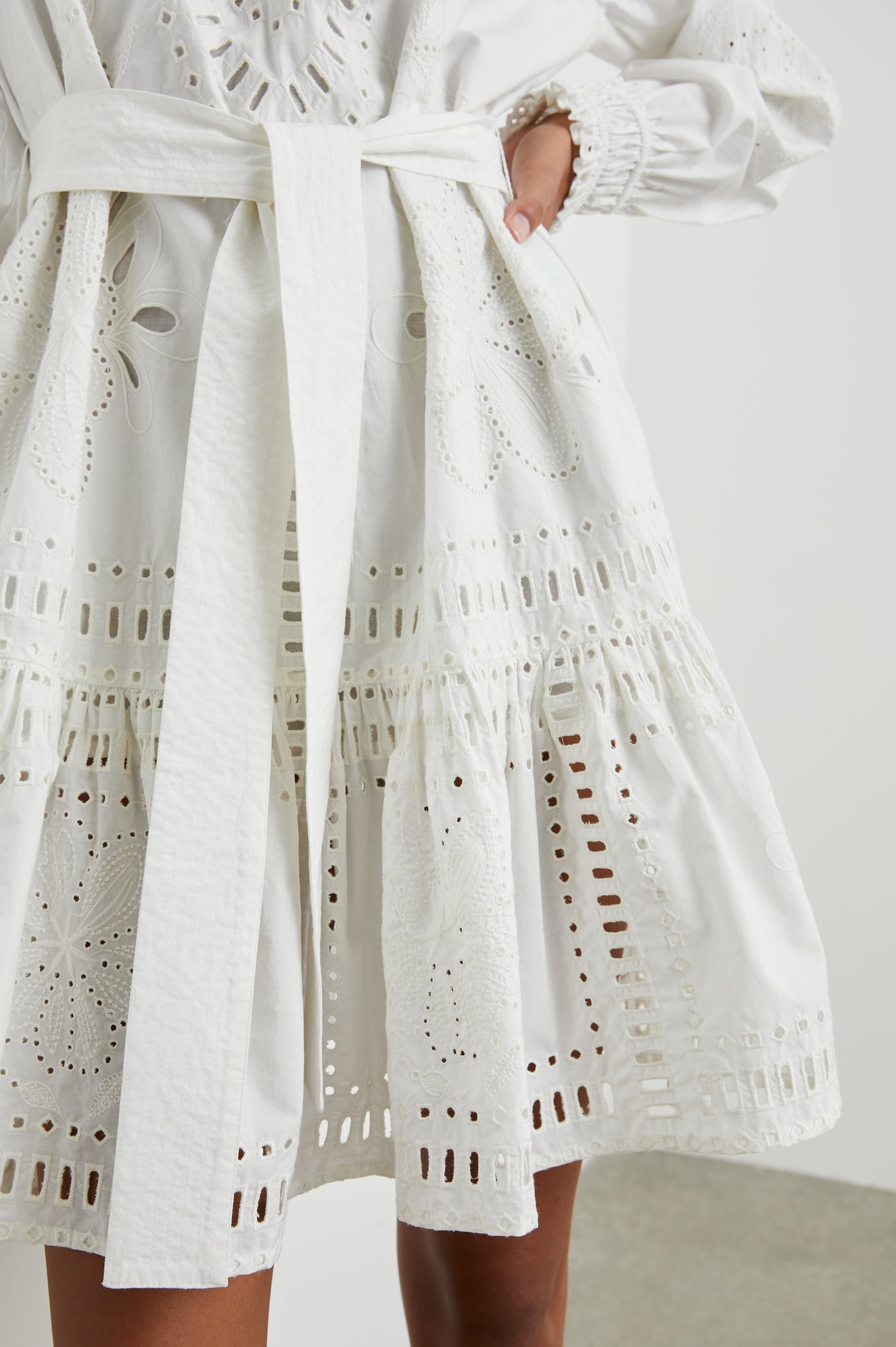 Saylor Long-Sleeve Midi Dress with a Half-Sealed Placket, a V Neck, Ruffled Collar with Shirring, a Fabric Tie Belt, and Floral and Geometric Eyelet Details in White Colorway - Front View Featured on Model 