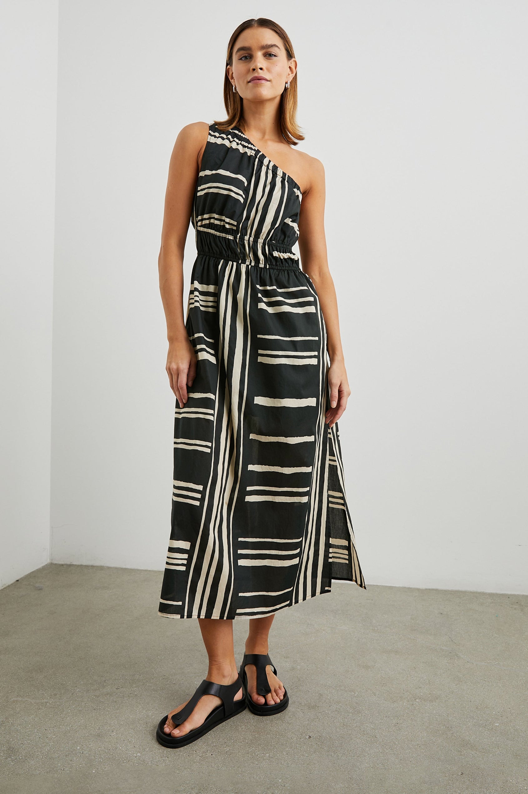 Selani Midi Dress With an Asymmetrical Neckline, Mid-Thigh Slide Slit and Cinched Waistband in Island Stripe Colorway, with alternating white and black horizontal and vertical stripes - Front Full Body View Featured on Model
