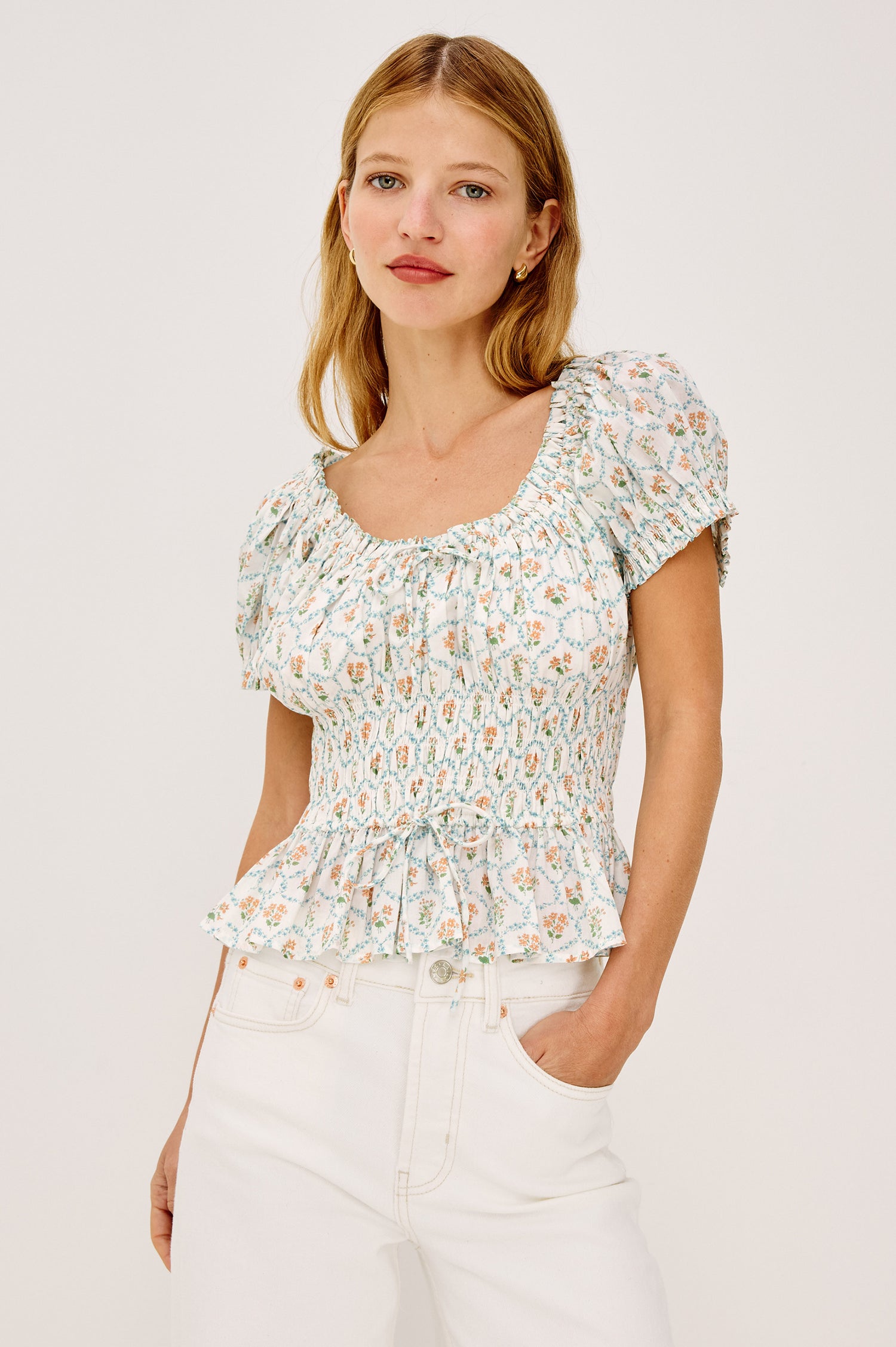 Serena Crop Top in Beach Cotton With Scoop Neckline, Short Puff Sleeves, Center-Front Ties, Smocked Waist, and Flared Peplum Hem in Peach Peony Colorway - Upper Body Front View Featured on Model
