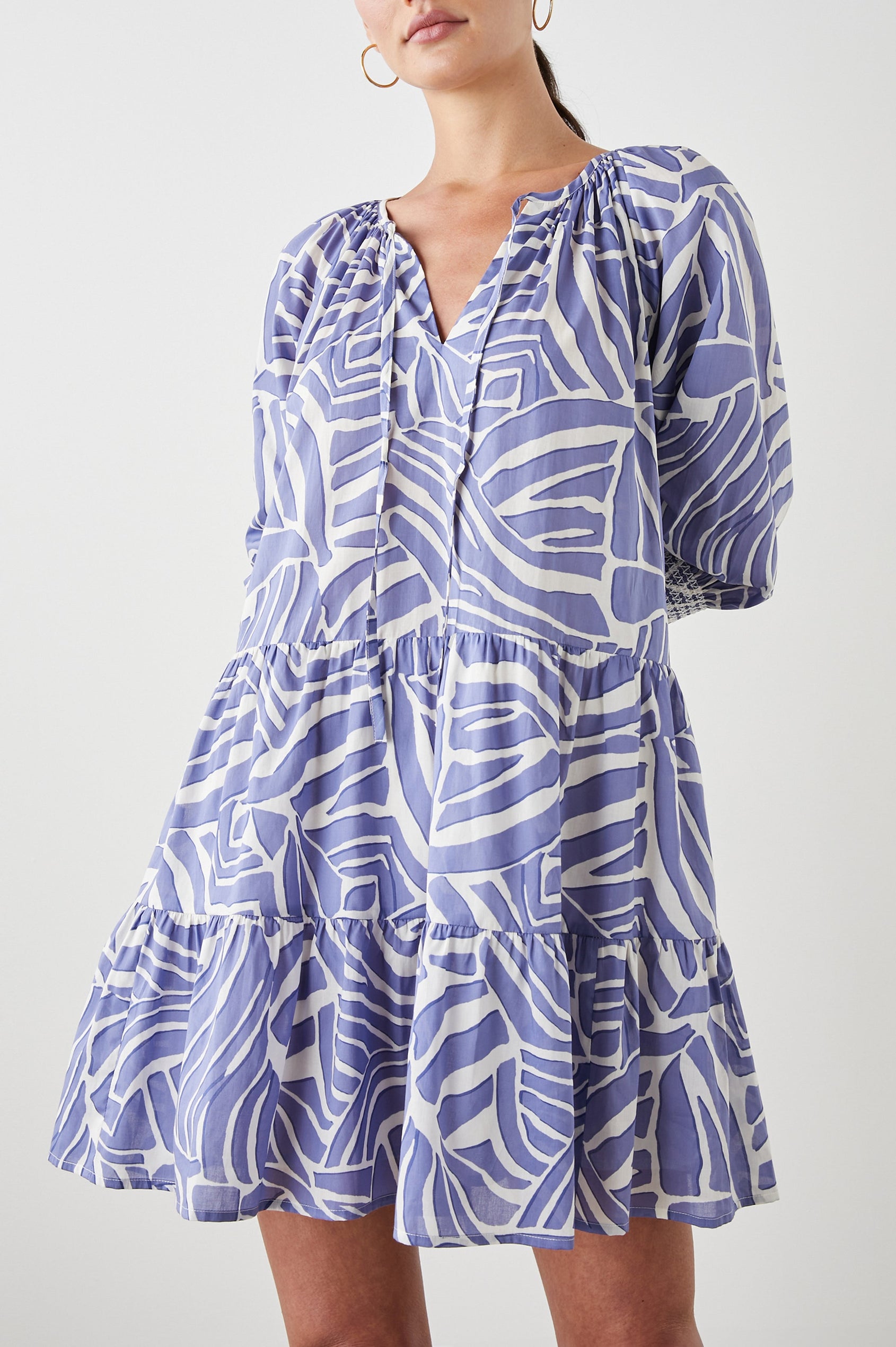 Sia Mini Dress with Three-Quarter Sleeves, Shirred Cuffs, a Tiered Skirt, and a V Neck with a Tie and Light Ruching in Island Waves Colorway, a Purple and White Print - Front View Featured on Model 