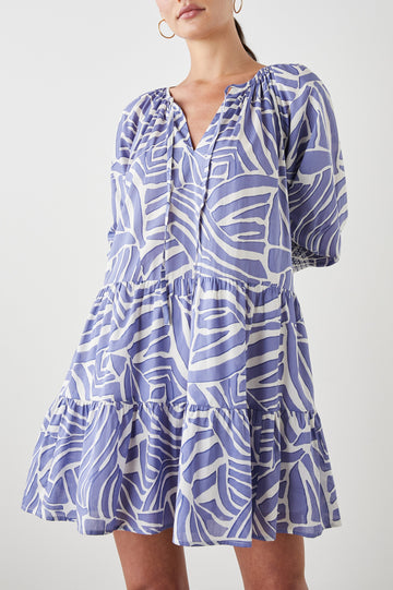 Sia Mini Dress with Three-Quarter Sleeves, Shirred Cuffs, a Tiered Skirt, and a V Neck with a Tie and Light Ruching in Island Waves Colorway, a Purple and White Print - Front View Featured on Model 