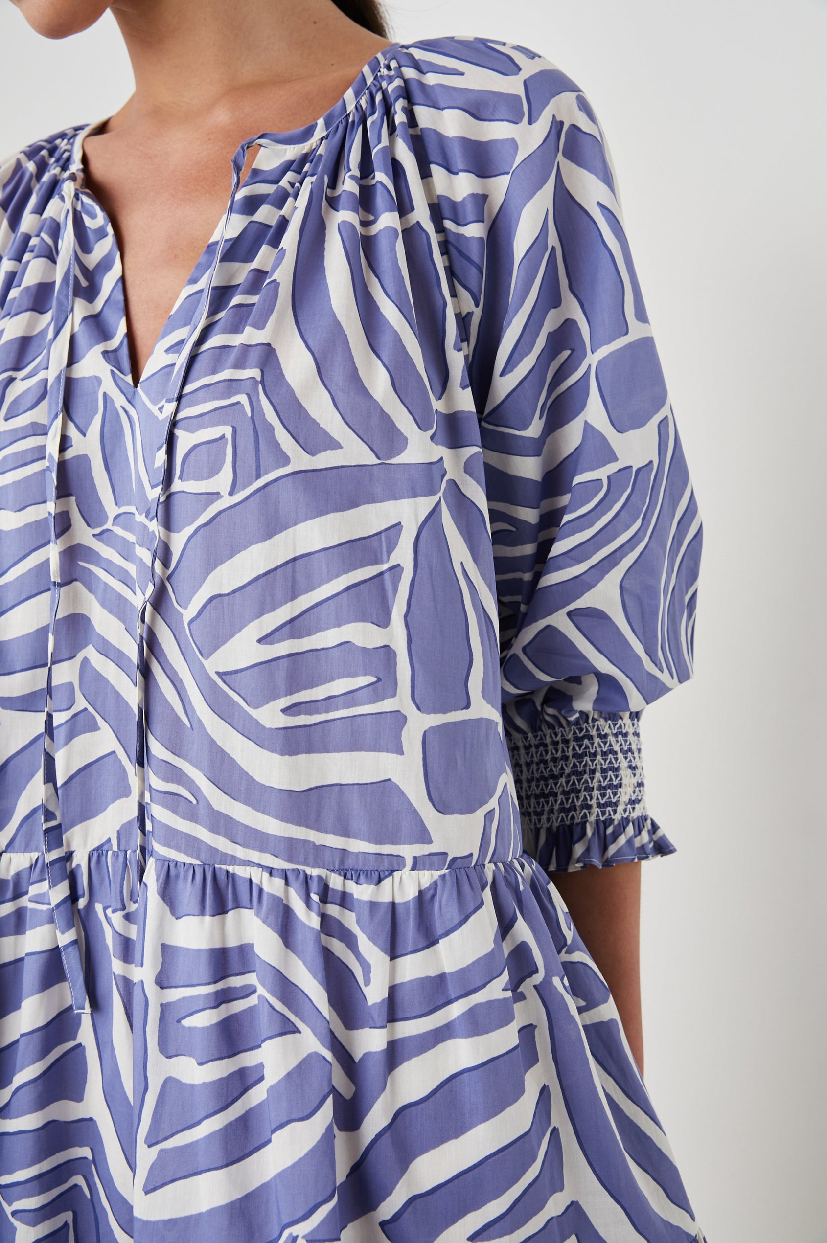 Sia Mini Dress with Three-Quarter Sleeves, Shirred Cuffs, a Tiered Skirt, and a V Neck with a Tie and Light Ruching in Island Waves Colorway, a Purple and White Print - Front View Featured on Model 