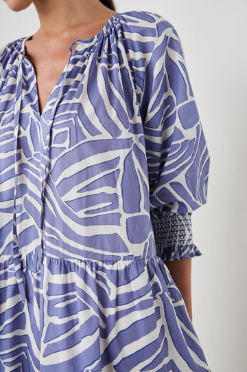 Sia Mini Dress with Three-Quarter Sleeves, Shirred Cuffs, a Tiered Skirt, and a V Neck with a Tie and Light Ruching in Island Waves Colorway, a Purple and White Print - Front View Featured on Model 