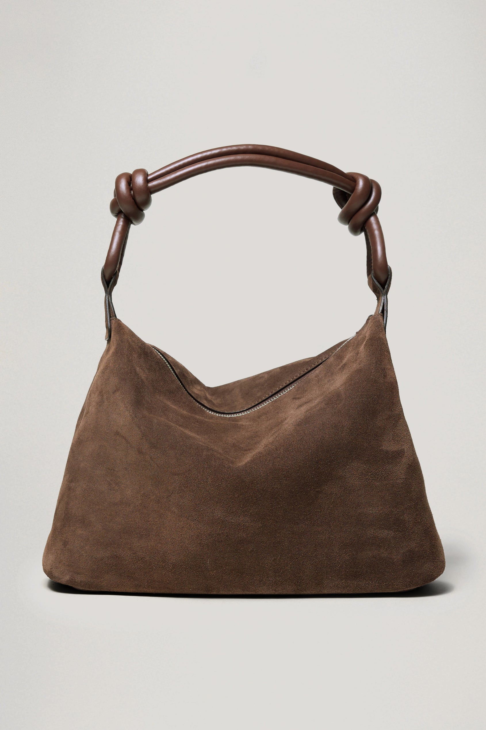 The Siena is a true slouchy hobo bag, crafted from smooth leather with a knotted top strap and a zip closure finished with a fringed tassel. In Espresso Suede Colorway. Front view featured.