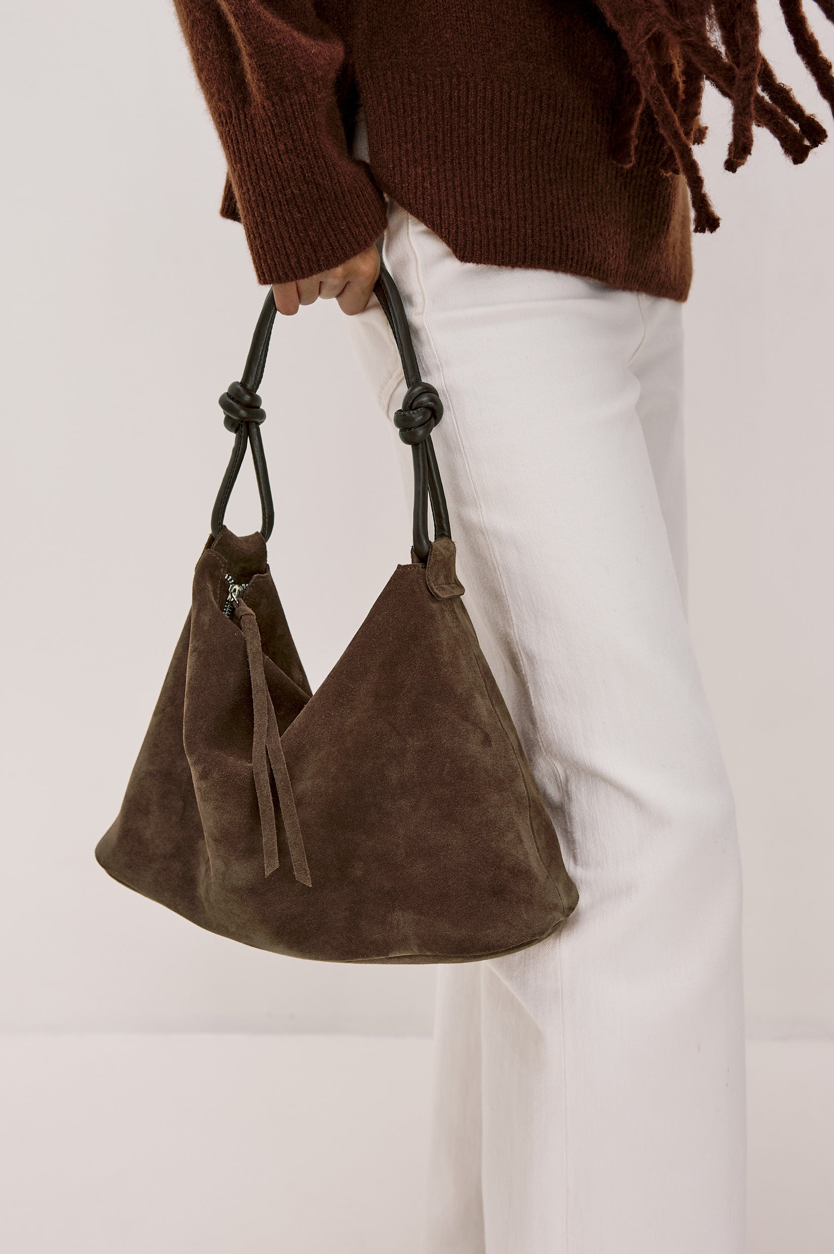 The Siena is a true slouchy hobo bag, crafted from smooth leather with a knotted top strap and a zip closure finished with a fringed tassel. In Espresso Suede Colorway. Full body side view featured on model.
