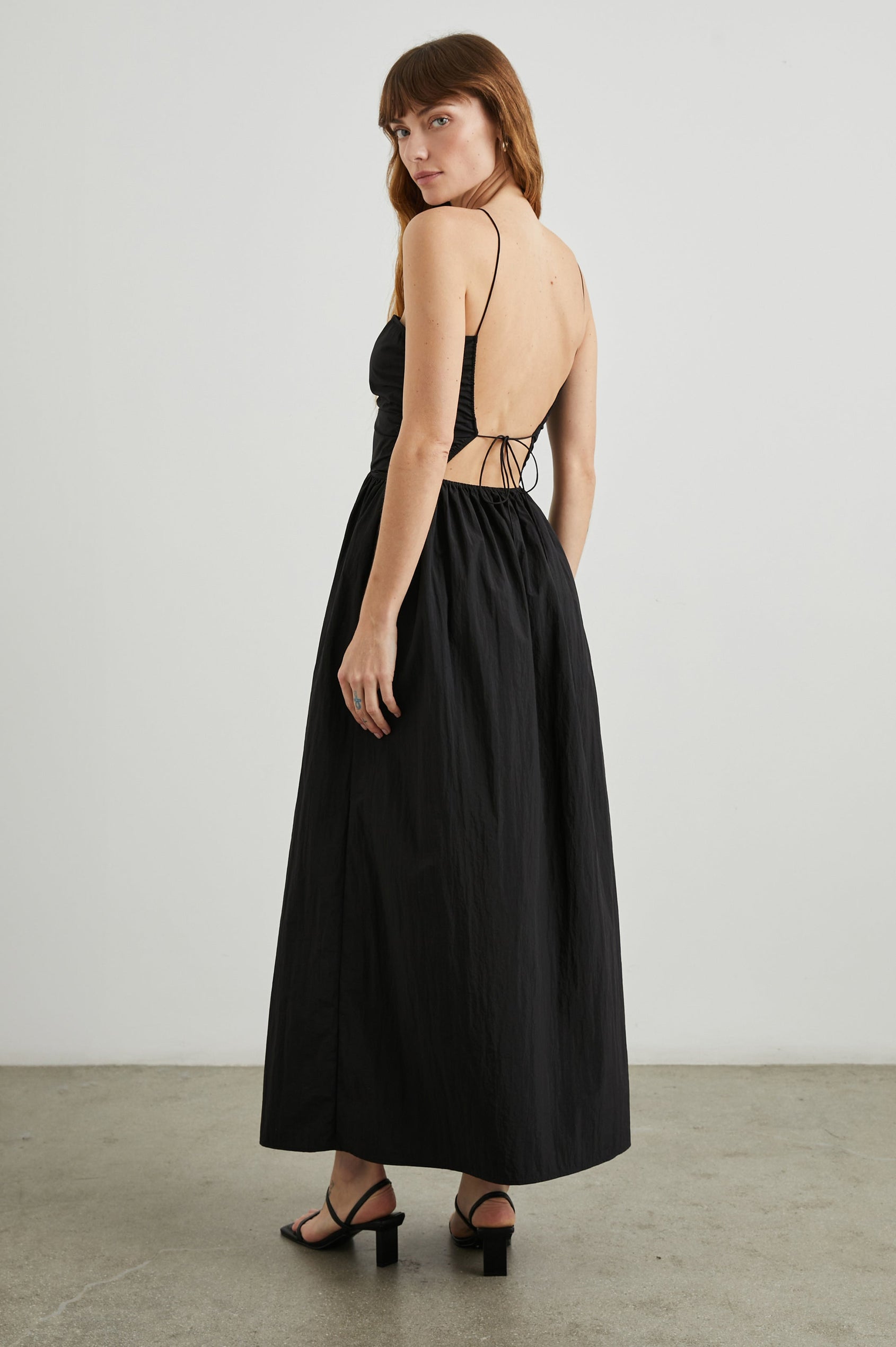 Silvia Sleeveless Maxi Dress with Spaghetti Straps with a Lower Back Tie, an Open Back, and Cutouts Along the Center of the Bodice in Black Nylon Colorway - Back Full Body View Featured on Model
