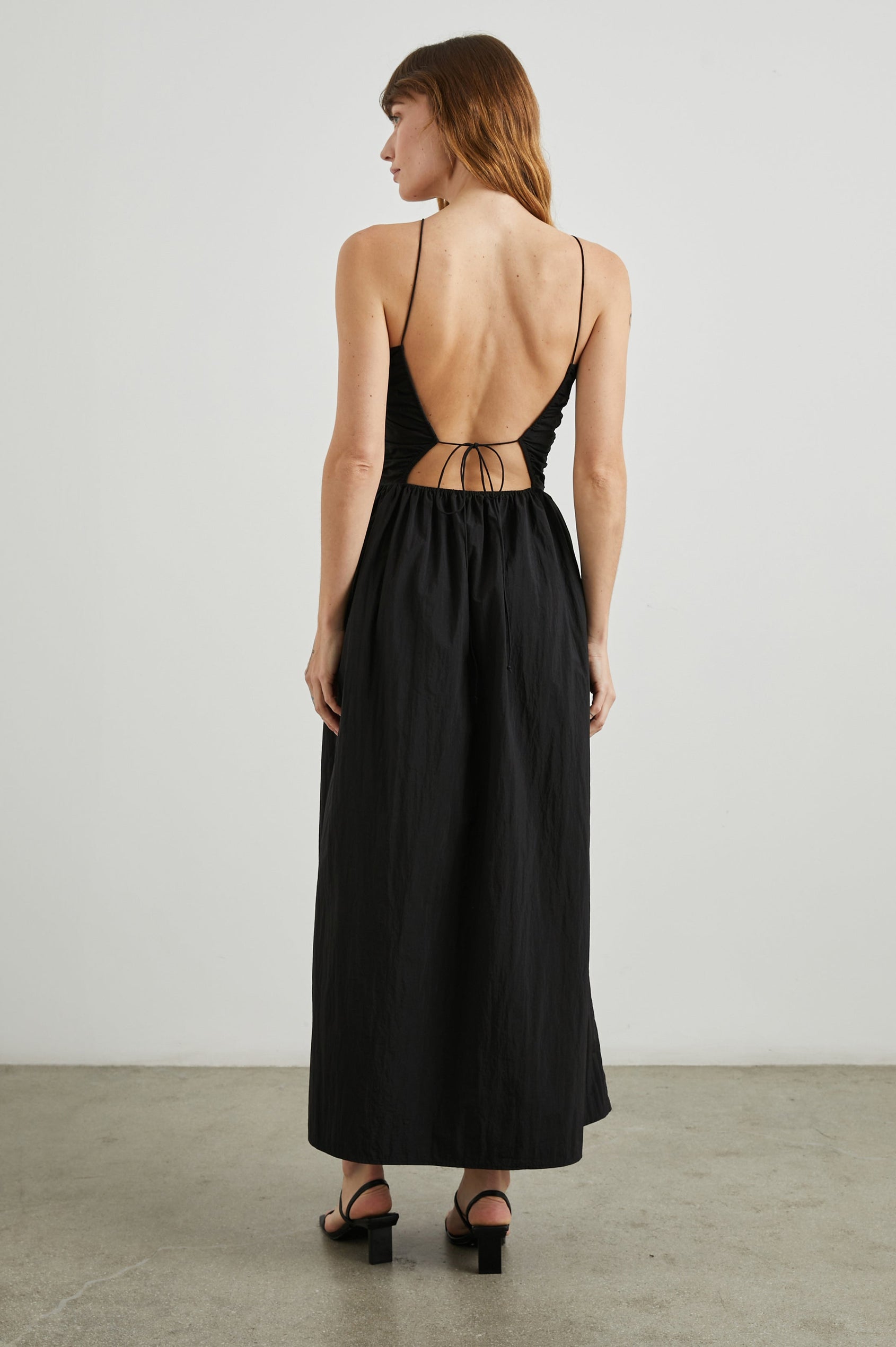 Silvia Sleeveless Maxi Dress with Spaghetti Straps with a Lower Back Tie, an Open Back, and Cutouts Along the Center of the Bodice in Black Nylon Colorway - Back Full Body View Featured on Model