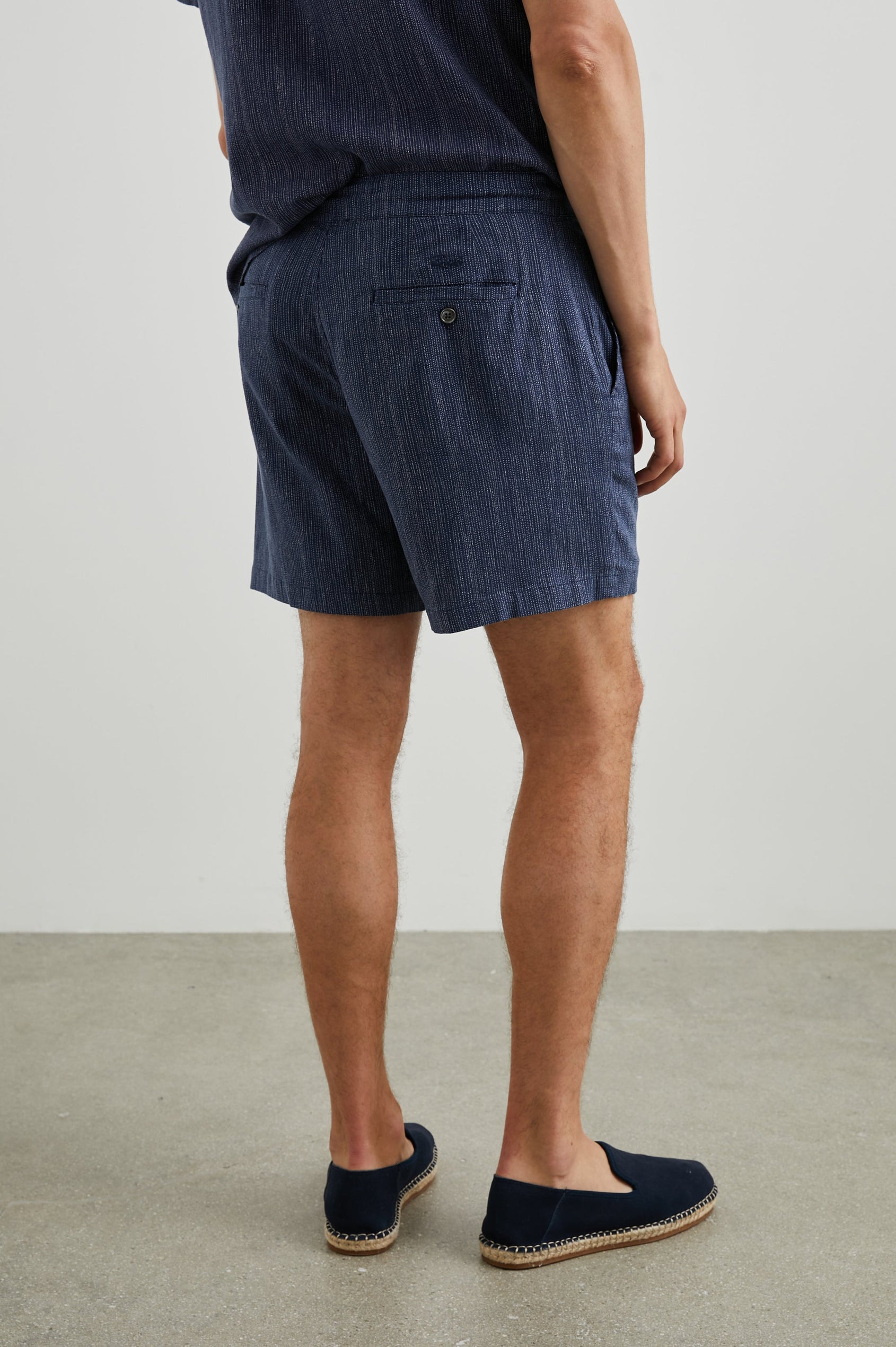 Sona Shorts with Two Front Pockets and Two Back Button Welt Pockets in Matrix Navy Pearl Colorway, Thin Pearl Dashed Vertical Lines on Navy - Back View Featured on Model 