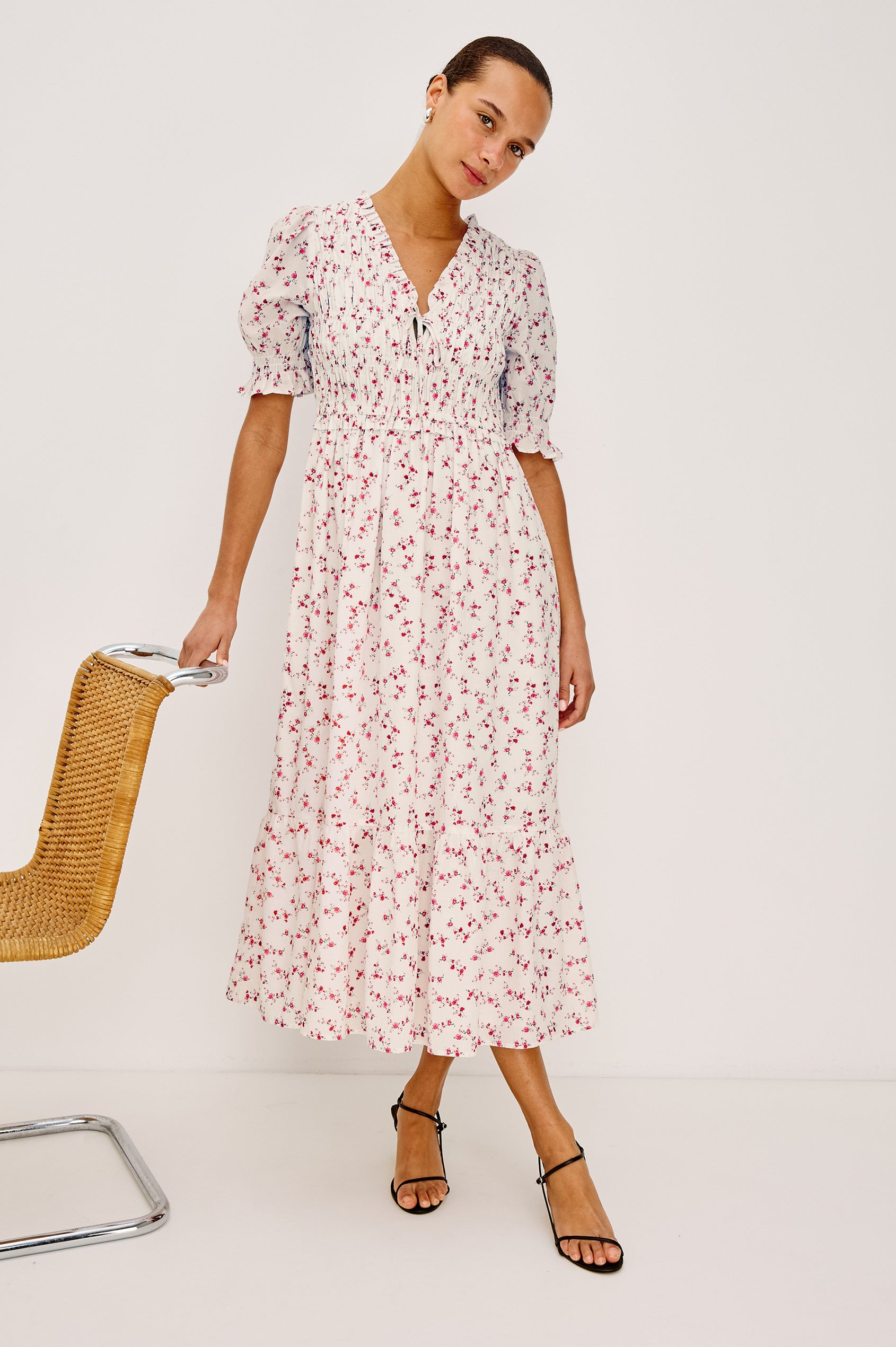 Sonica Midi Dress in Cotton With Fitted Smocked Bodice Plunging V-Neckline With Self-Ties Short Puff Sleeves and Single Tiered A-Line Skirt in Rouge Romantic Colorway - Full Body Front View Featured on Model Sitting