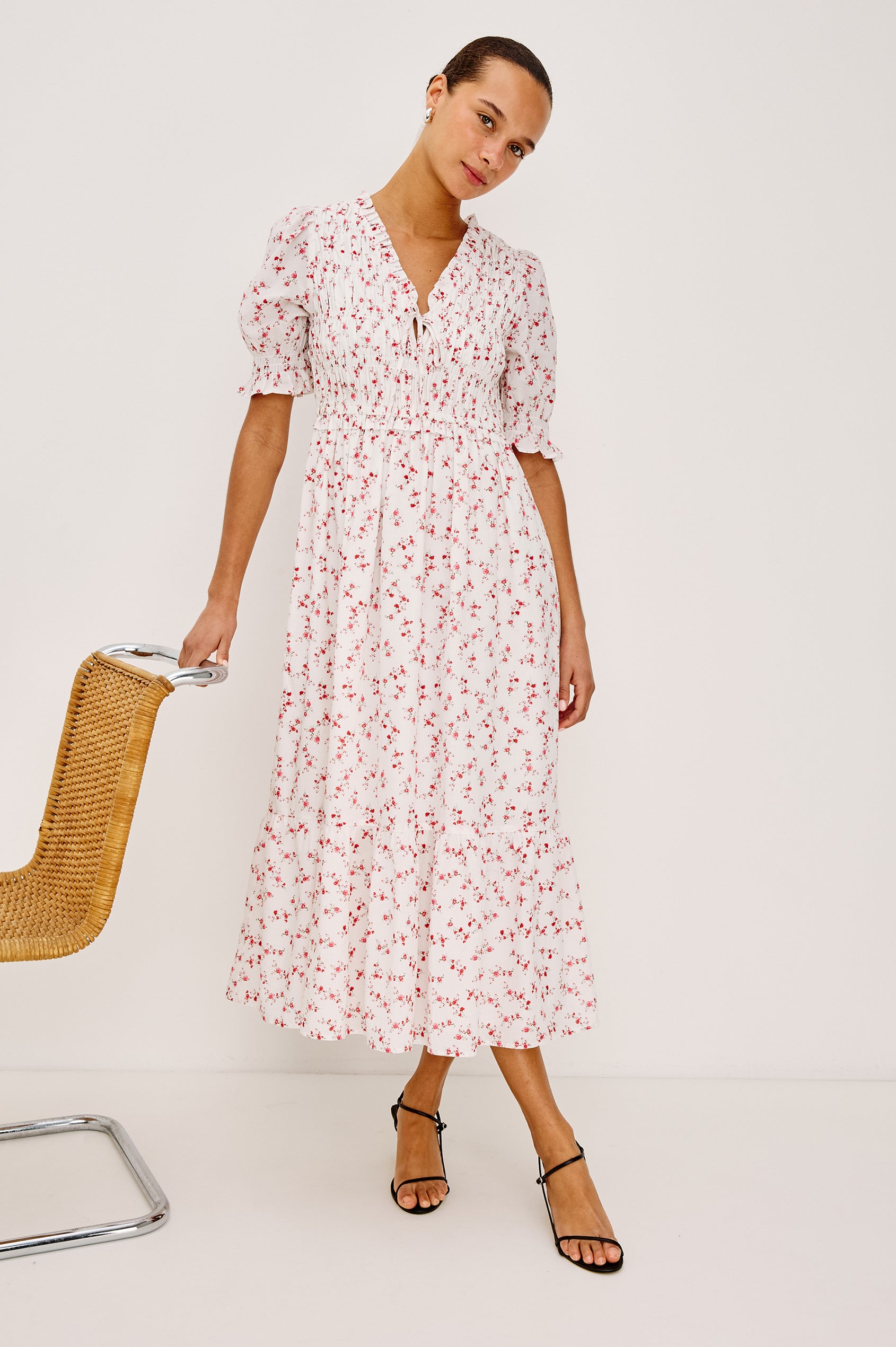 Sonica Midi Dress in Cotton With Fitted Smocked Bodice Plunging V-Neckline With Self-Ties Short Puff Sleeves and Single Tiered A-Line Skirt in Rouge Romantic Colorway - Full Body Front View Featured on Model Sitting