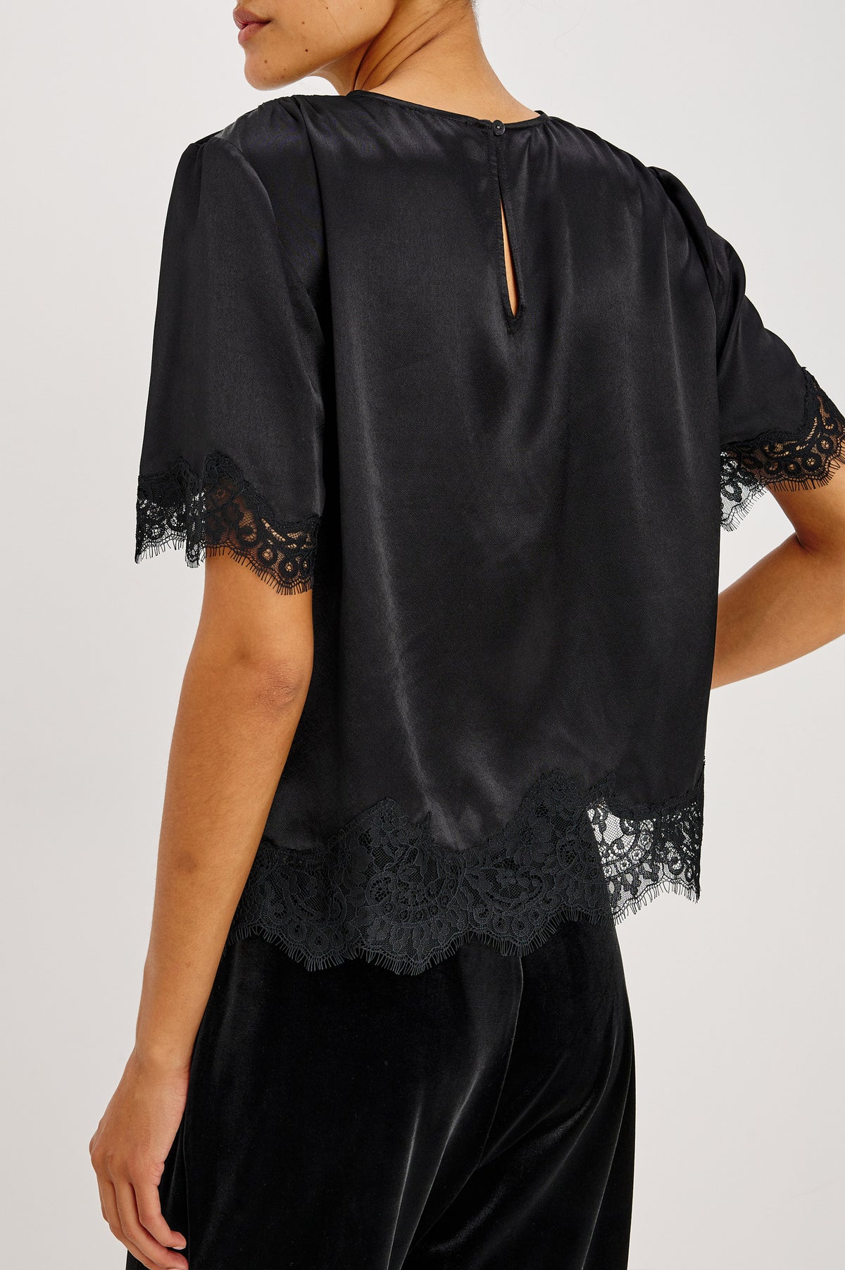 Sonora Shirt in Satin Crepe With Crew Neckline, Loose Boxy Fit, Shirred Shoulders, Short Sleeves, Button-Loop Back Keyhole, and Lace Trim in Black Colorway - Upper Body Back View Featured on Model