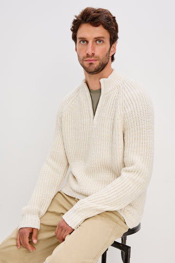Stratton is a quarter-zip long sleeved sweater knitted from chunky cotton blend knit in Snowdrift Marl colorway. Front seated view featured on model.