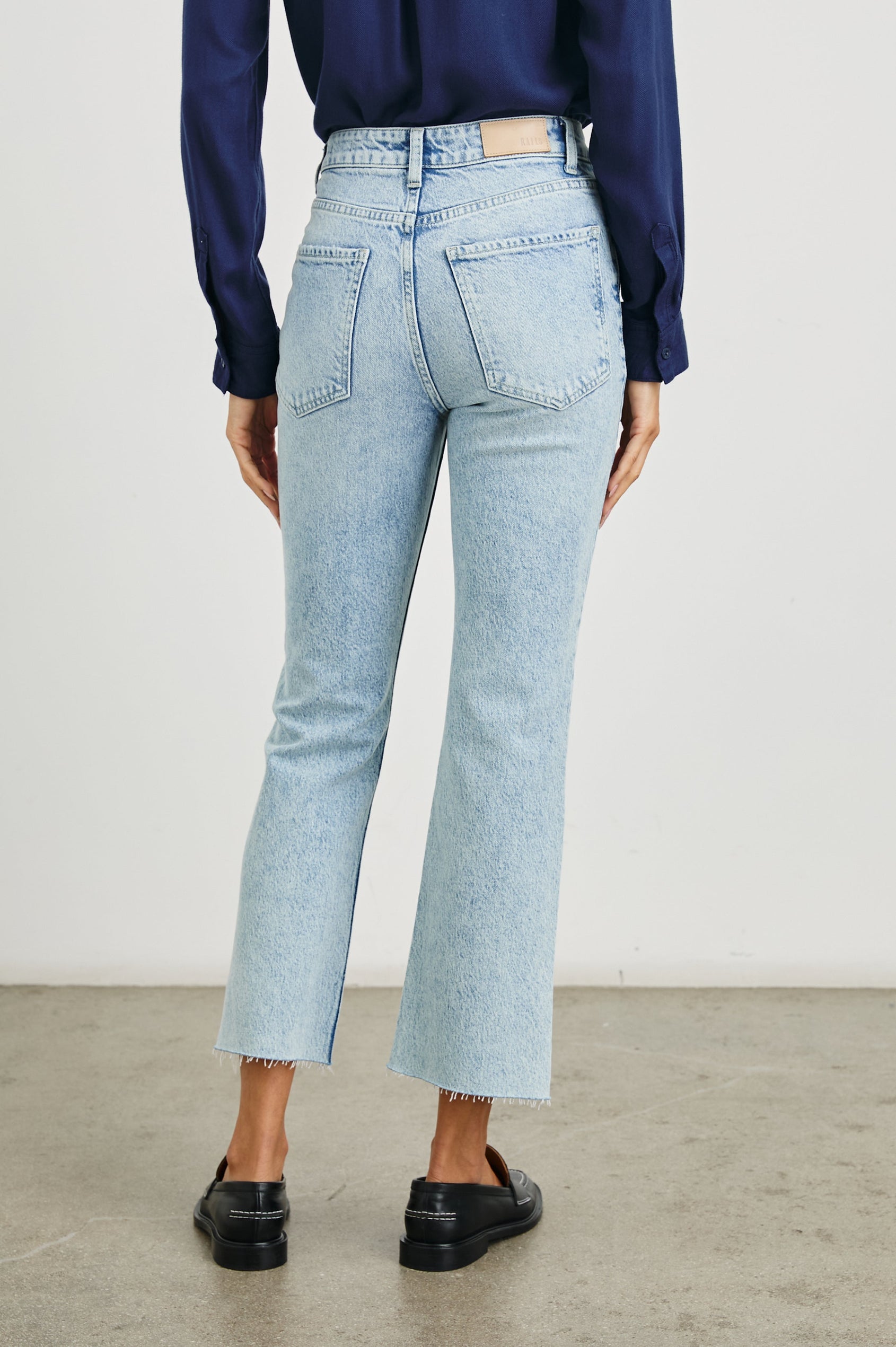 Sunset Crop Slim Fare Jeans with a Raw Hem, Belt Loops, Two Front Pockets plus a Coin Pocket and Two Back Patch Pockets in Snowbird Colorway - Back View Featured on Model