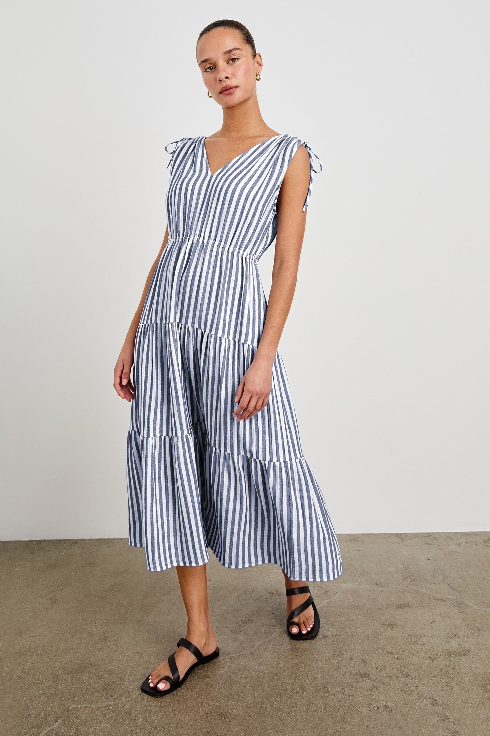 Front view of model wearing a tiered midi dress featuring blue and white vertical stripes. Suzette dress features an elasticated waist and customizable shoulder straps.