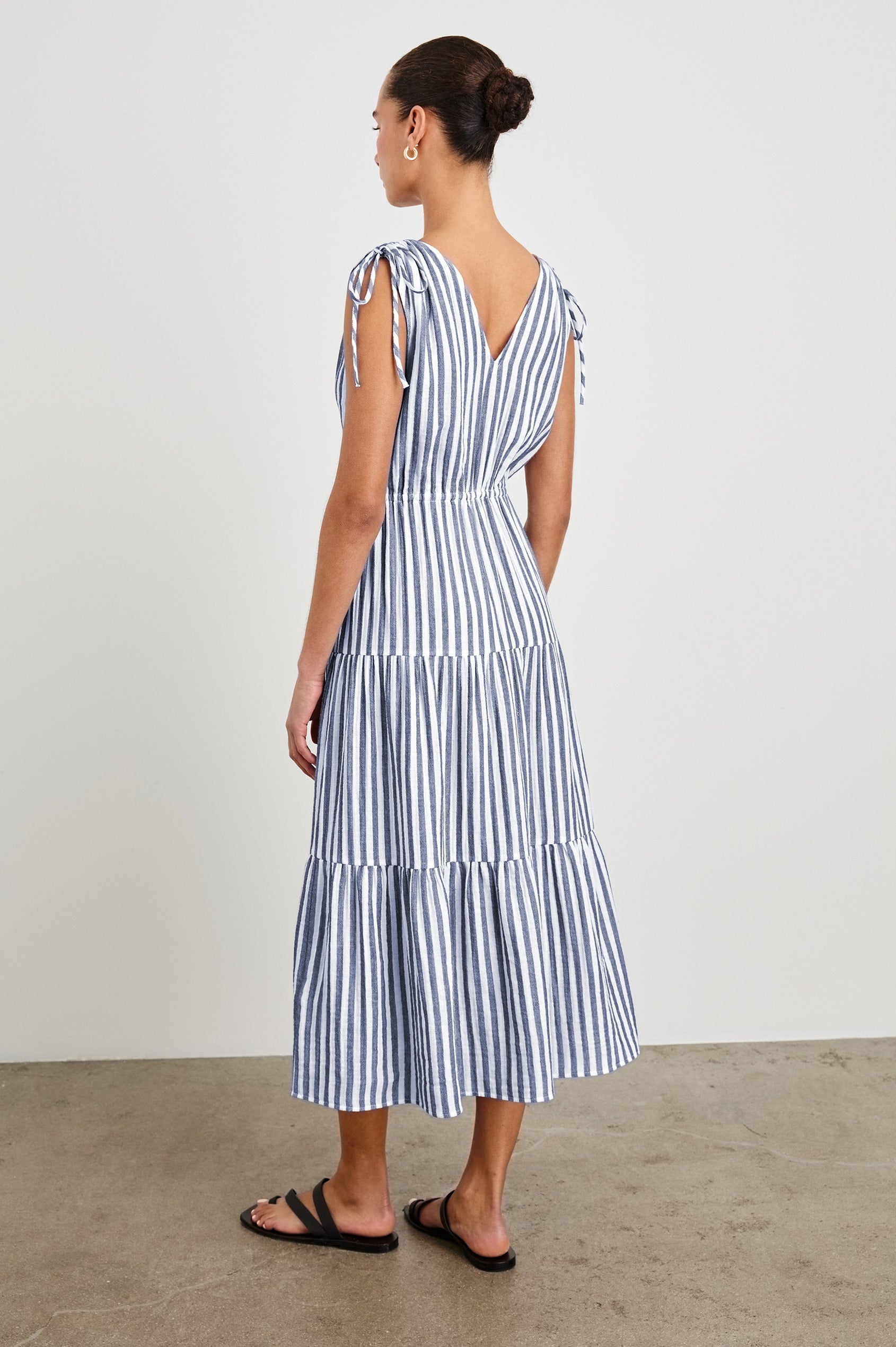 Back view of model wearing a tiered midi dress featuring blue and white vertical stripes. Suzette dress features an elasticated waist and customizable shoulder straps.