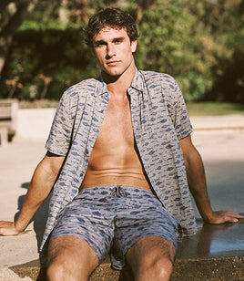 Man wearing a patterned shirt and shorts sitting outdoors.