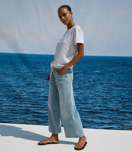 Woman standing by the ocean wearing a white t-shirt and light blue jeans.