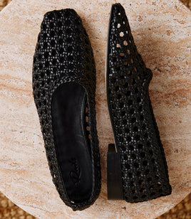 A pair of black woven pointed-toe flats shown from top and side views on a round stone slab.