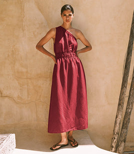 Woman wearing a burgundy one-shoulder dress against a beige wall.