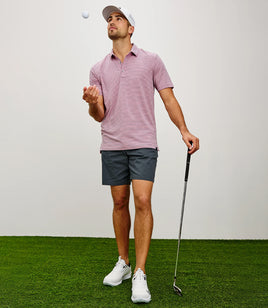 Man in golf attire preparing to hit a golf ball on a green surface with a white background
