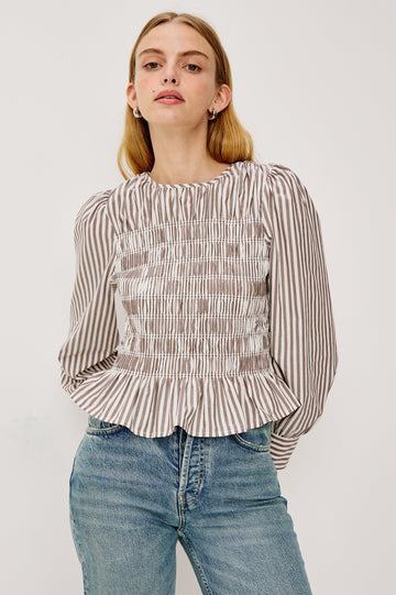 Tabi is a long sleeve crew neck top with puff sleeves and buttons at cuff, the bodice is pleated with a peplum hem in an Espresso Ivory Stripe colorway. Front view featured on model.
