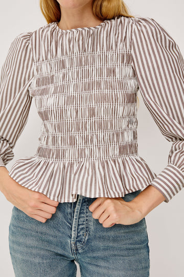 Tabi is a long sleeve crew neck top with puff sleeves and buttons at cuff, the bodice is pleated with a peplum hem in an Espresso Ivory Stripe colorway. Close Up view featured on model.
