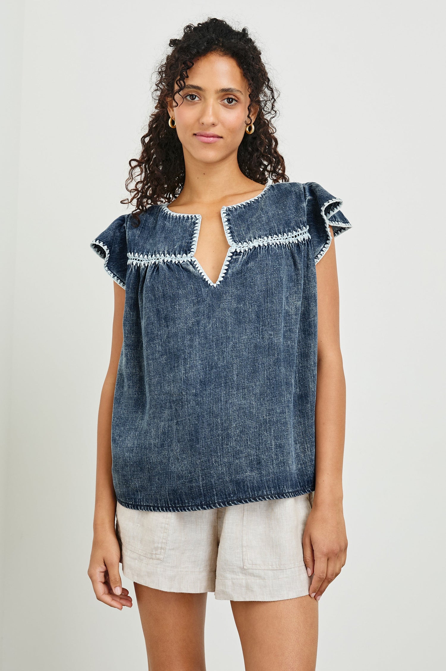 Tafia Top with an Open V-neck, Short Ruffle Cap Sleeves, and a White Blanket Stich along the Neckline, Cuffs and Yoke Seam in Classic Blue Colorway - Front Untucked View Featured on Model