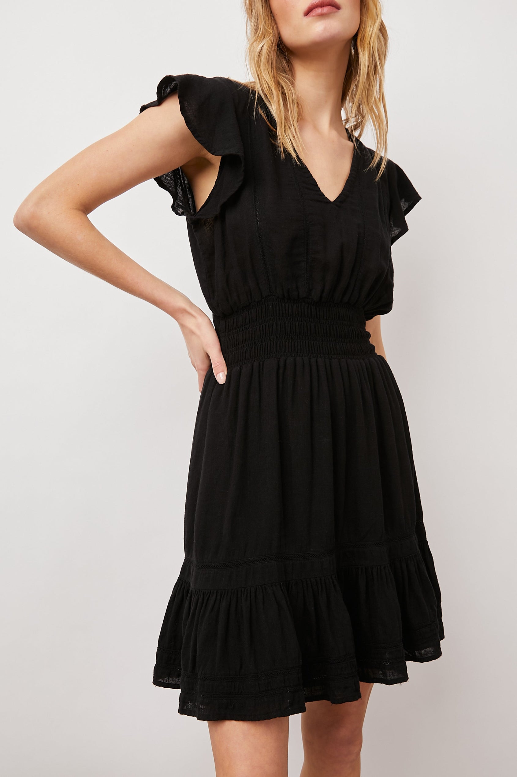 Tara Short Sleeve, Above the Knee Dress with a Smocked Waist, V Neck, Flutter Cap Sleeves, and Tiered Skirt with a Ruffled Hem in Black Lace Detail Colorway, with Vertical Lace Inserts on the Bodice and Horizontal Inserts on the Skirt - Front View Featured on Model 