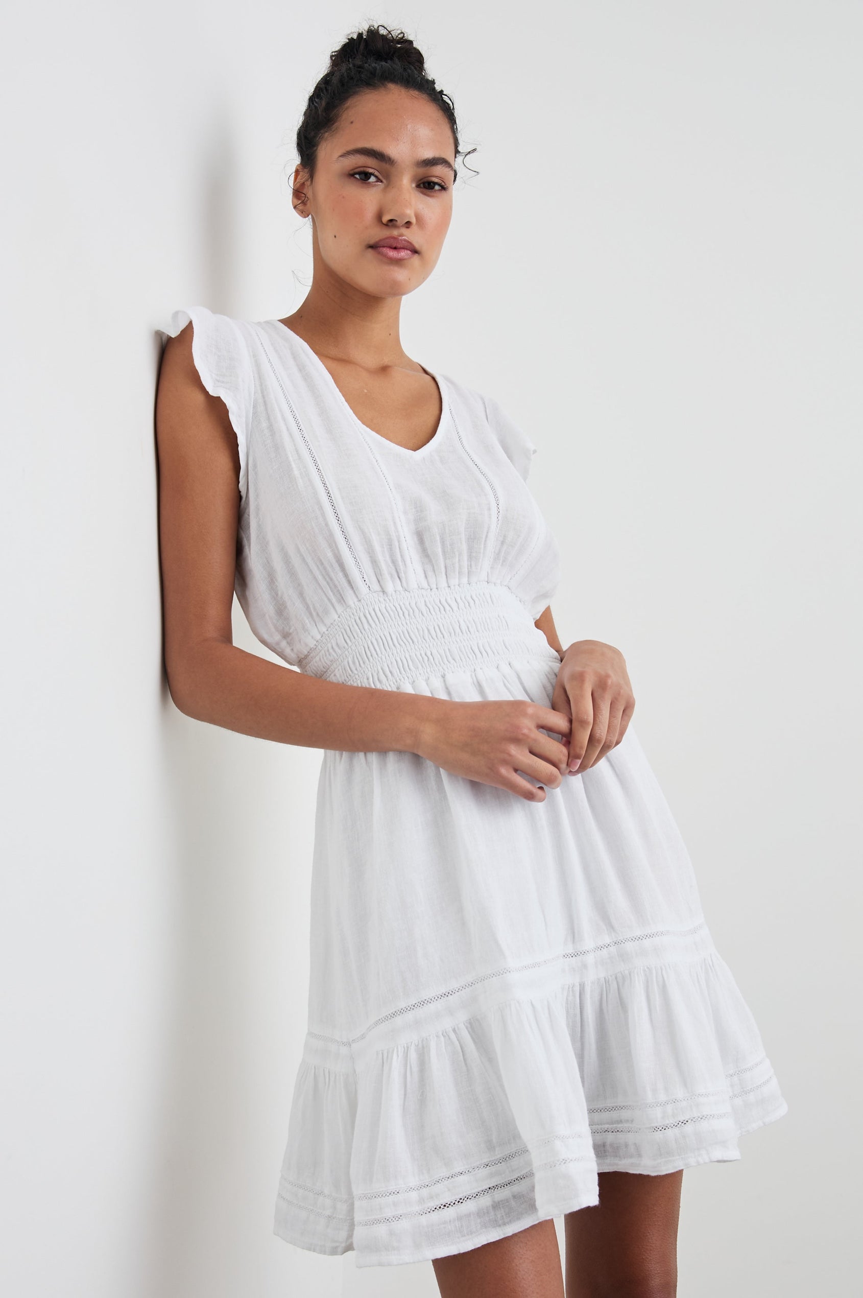 Tara Short Sleeve, Above the Knee Dress with a Smocked Waist, V Neck, Flutter Cap Sleeves, and Tiered Skirt with a Ruffled Hem in White Lace Detail Colorway, with Vertical Lace Inserts on the Bodice and Horizontal Inserts on the Skirt - Front View Featured on Model 