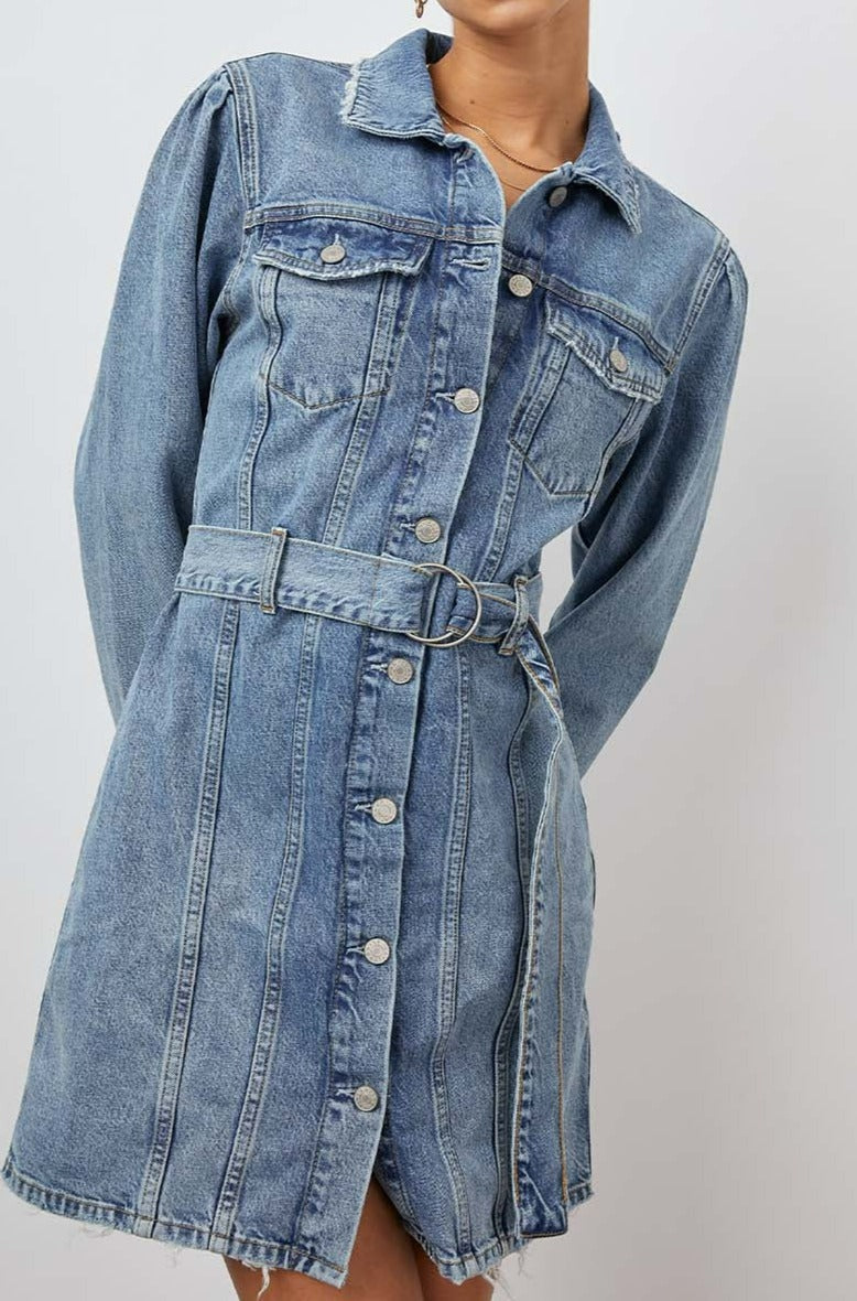 Griffith Long-Sleeve Denim Mini Dress with Buttons Down the Front, a Fabric Double Ring Belt, Two Chest Button Flap Pockets, Frayed Trim and Vertical Seams Down the Front in Indigo Charm Colorway - Front View Featured on Model 