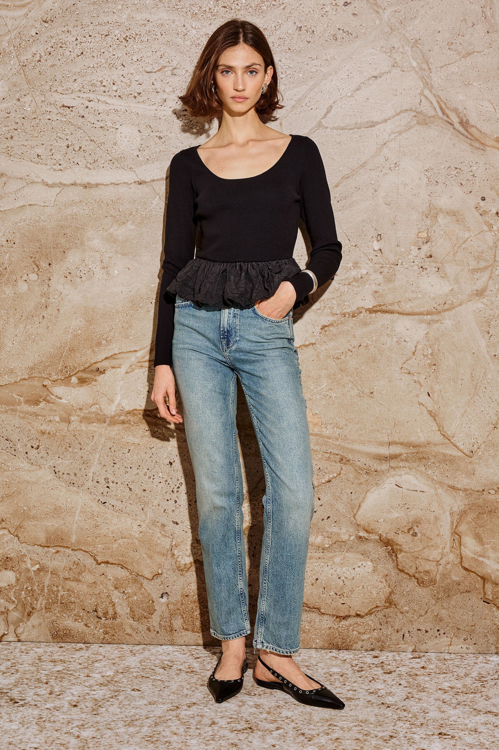 The Tillie is a fitted, long-sleeved sweater top with a contrasting cotton poplin ruffle at the hem in Black Colorway - Stylized full body front view featured on model