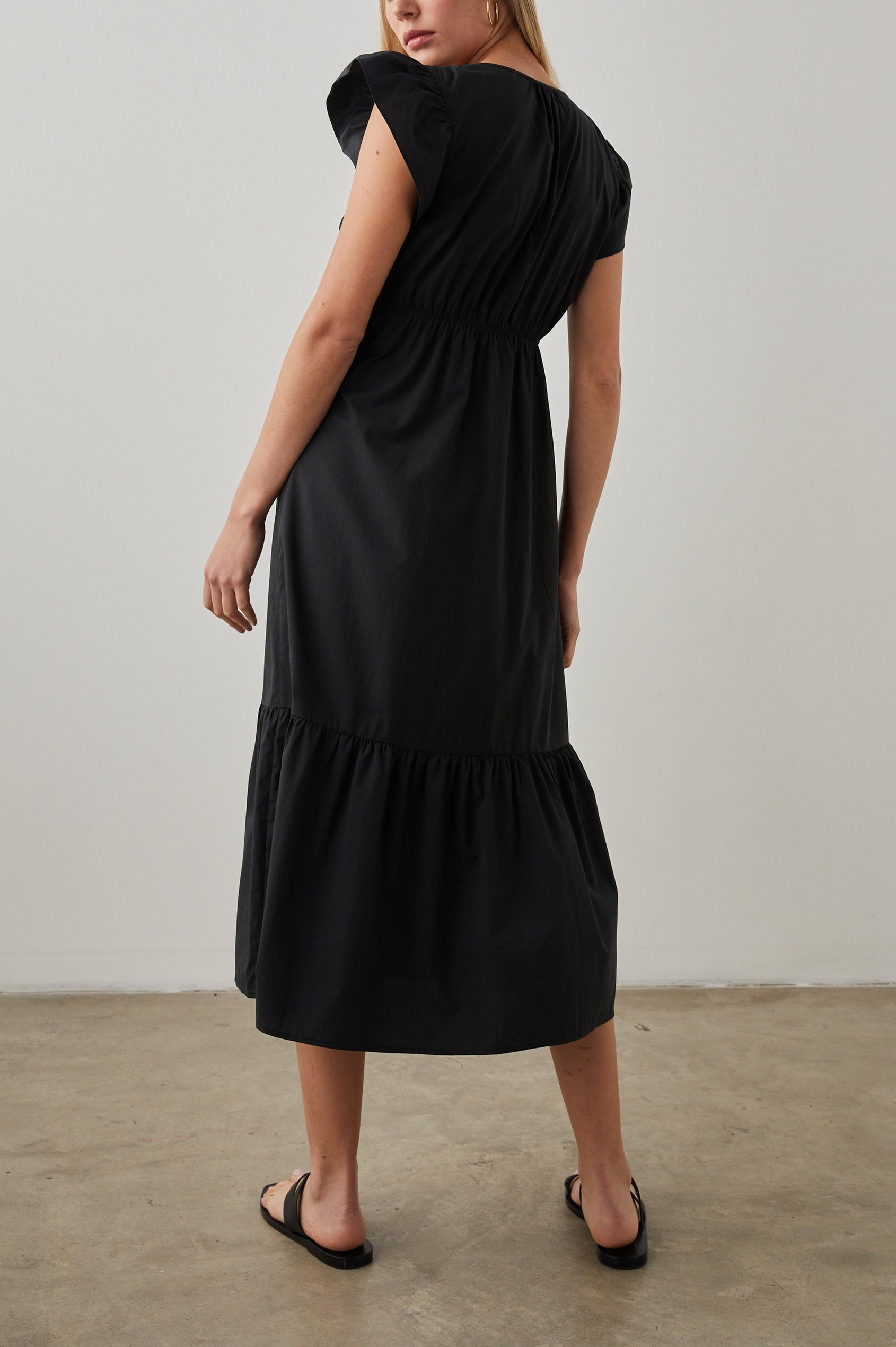 Tina Short Sleeve Midi Dress with Flutter Sleeves, a Deep V Neck with a Cutout and a Tiered Skirt in Black Colorway - Back Full Body View Featured on Model 