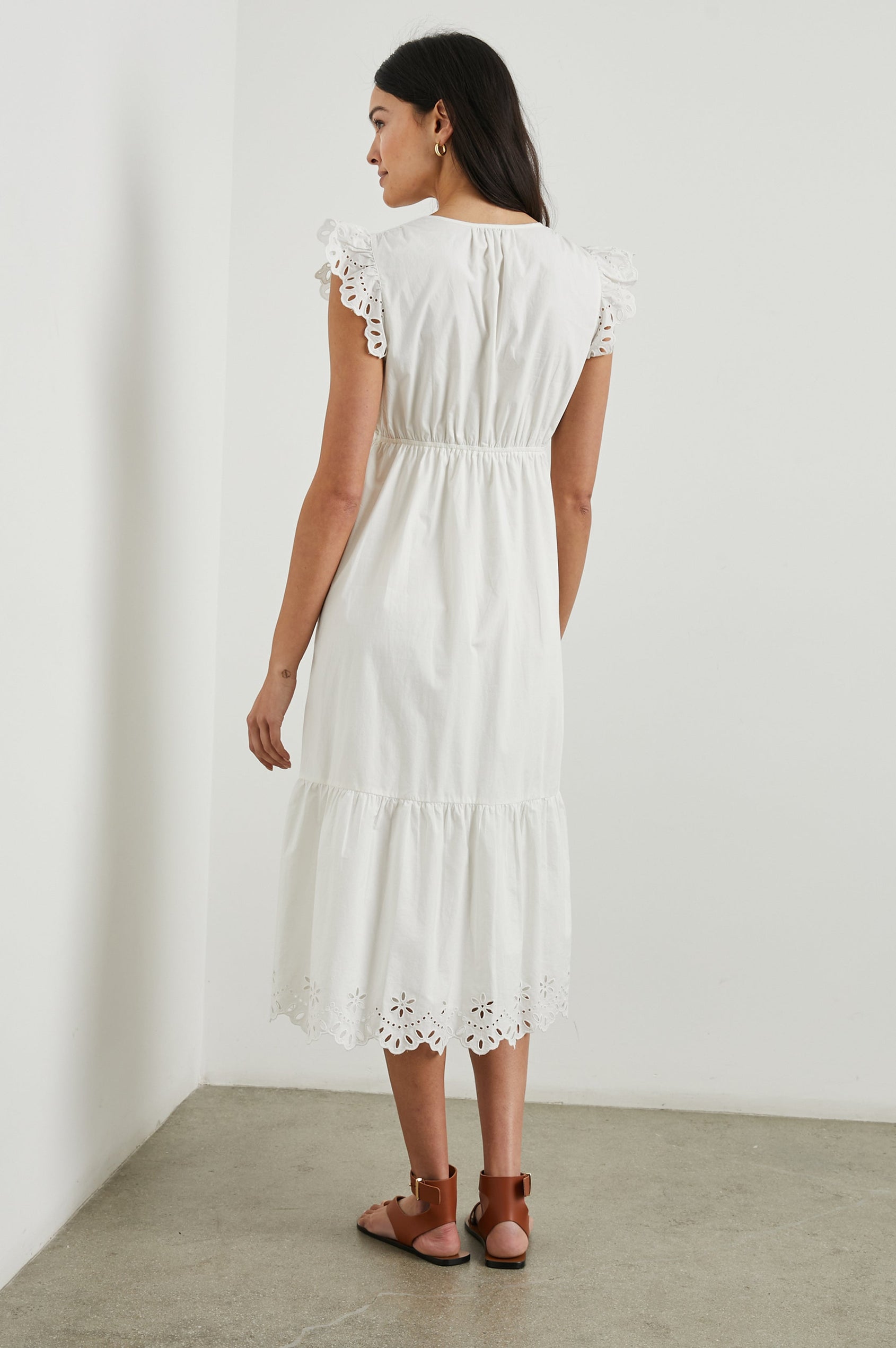Tina Short Sleeve Midi Dress with Flutter Sleeves, a Deep V Neck with a Cutout and a Tiered Skirt in White Colorway, with eyelets on the Sleeves and an Eyelet Floral Pattern on the Hem - Back Full Body View Featured on Model 