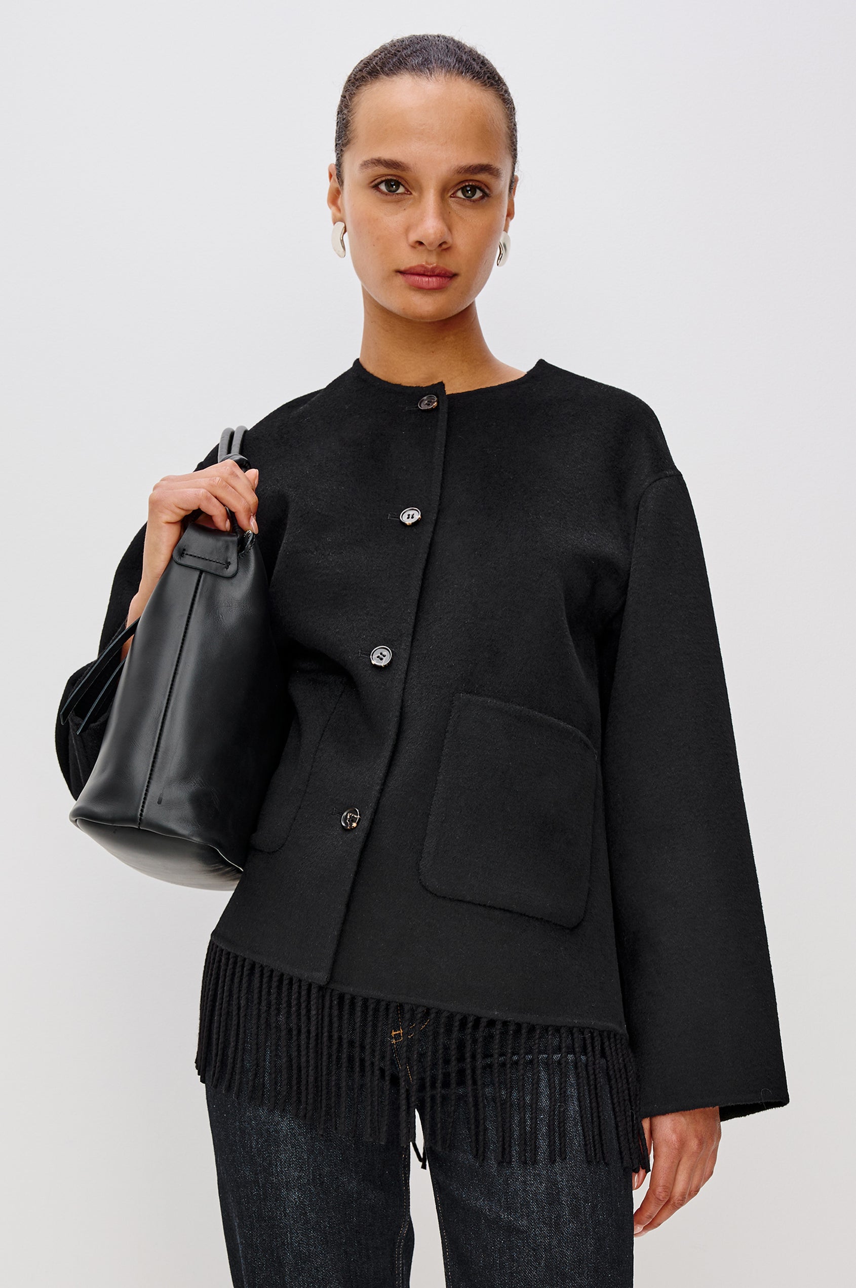 A heavyweight black wool-blend jacket with a relaxed fit. The jacket includes front button closures, patch pockets, and fringe detail at the hem for added texture and style. Front View Featured on Model.