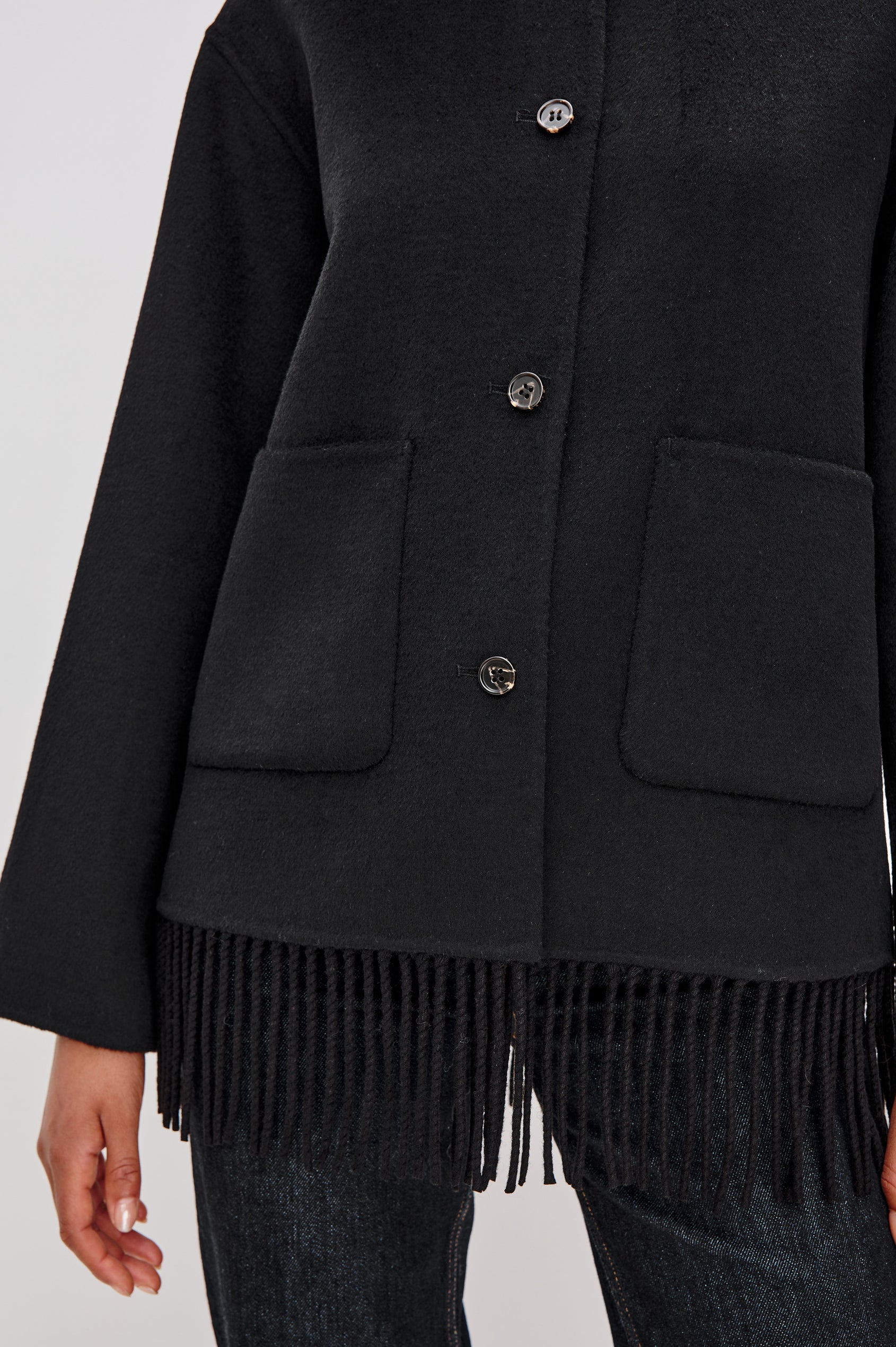 Tomoko Jacket in Heavyweight Wool Blend With Front Buttons, Patch Pockets, Relaxed Fit, Long Sleeves, and Fringe Hem in Black Colorway - Mid Body Front Close Up View Featured on Model