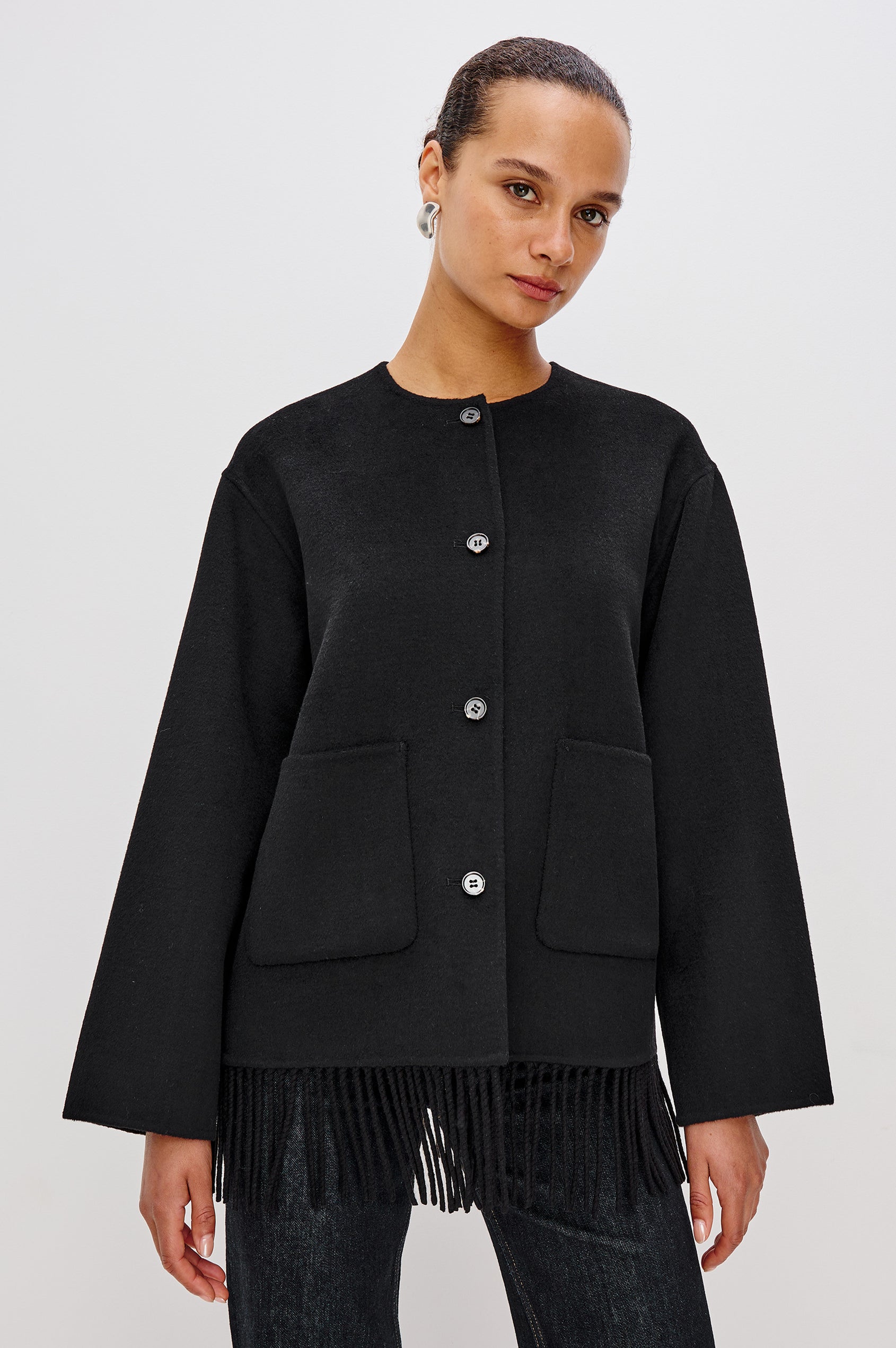 A heavyweight black wool-blend jacket with a relaxed fit. The jacket includes front button closures, patch pockets, and fringe detail at the hem for added texture and style. Front View Featured on Model.