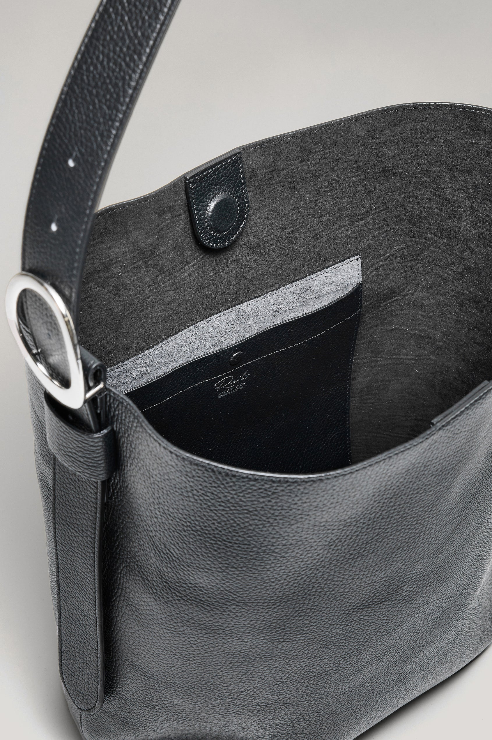 Torino Bucket Bag in Italian Pebbled Leather With Adjustable Strap and Polished Silver Oval Buckle, Microsuede Lining, Interior Magnetic Closure, Snap Button-Slip Pocket, and Subtle Branded Detailing in Black Colorway - Top Interior View Featured