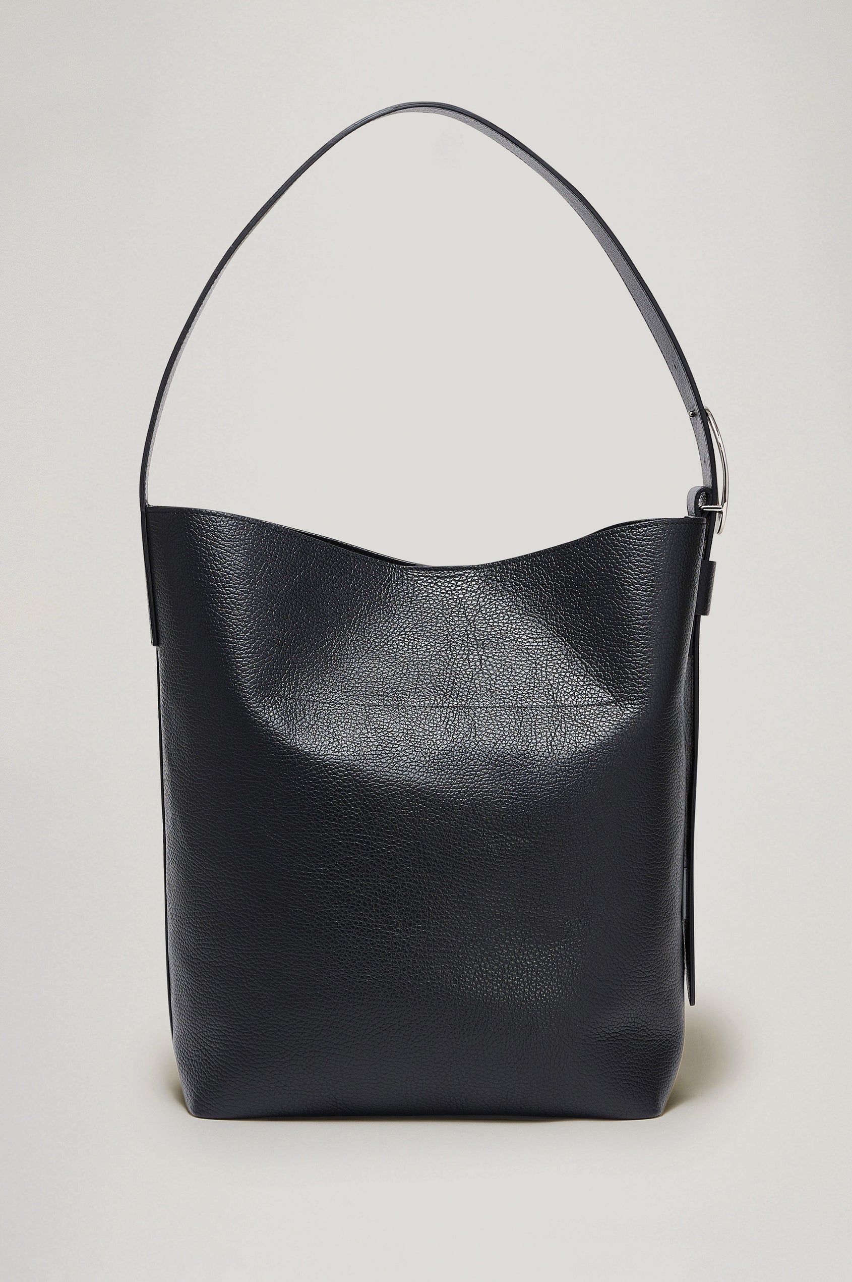 The Torino is a soft pebbled leather bucket bag, designed with an adjustable strap and polished silver oval buckle, in black colorway. Detailed view of buckle featured.