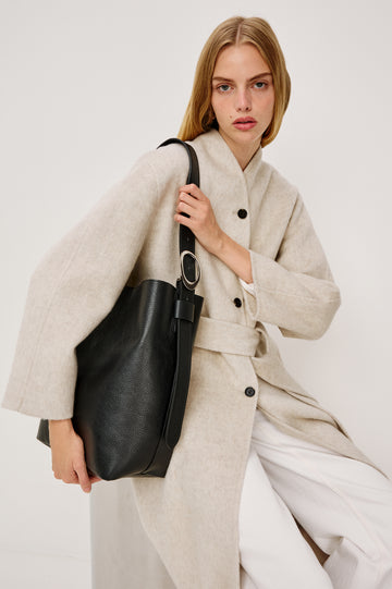 The Torino is a soft pebbled leather bucket bag, designed with an adjustable strap and polished silver oval buckle, in black colorway. Side view featured on model.