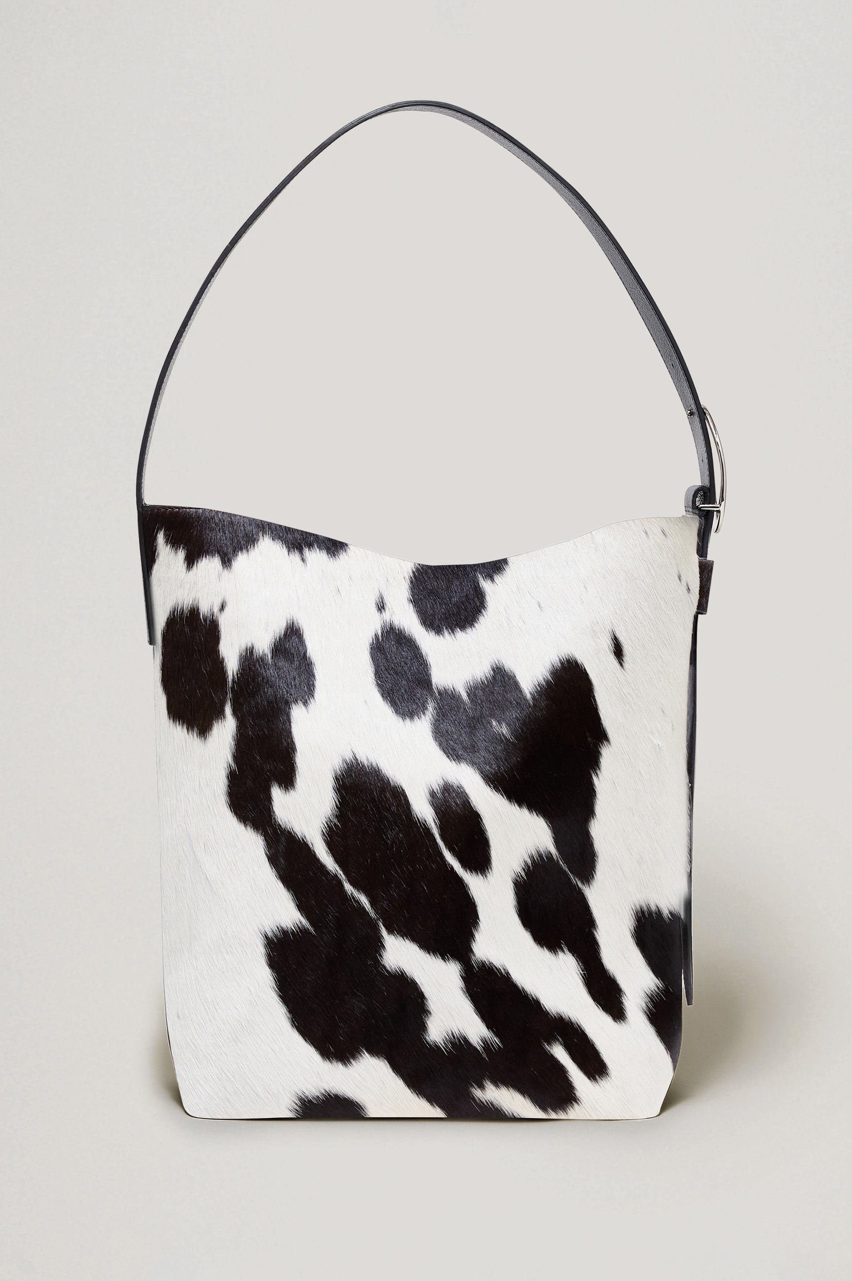 Torino Bucket Bag in Cow Print Haircalf With Adjustable Strap and Polished Silver Oval Buckle, Microsuede Lining, Interior Magnetic Closure, Snap Button-Slip Pocket, and Subtle Branded Detailing in Cowgirl Haircalf Colorway Colorway - Side Close Up View Featured