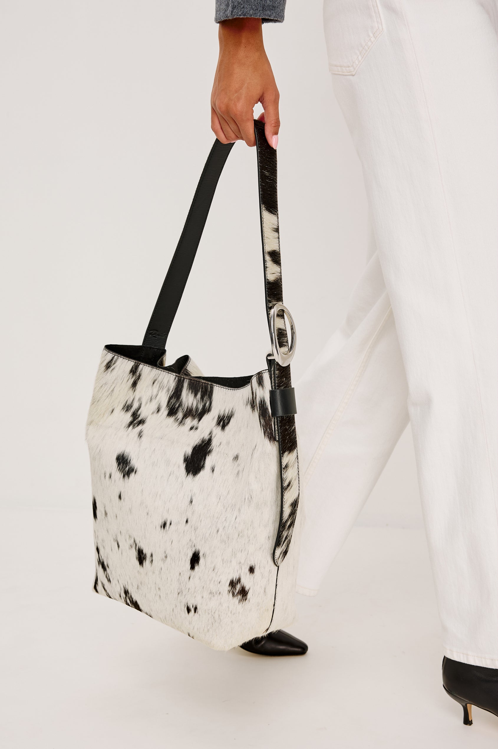 Torino Bucket Bag in Cow Print Haircalf With Adjustable Strap and Polished Silver Oval Buckle, Microsuede Lining, Interior Magnetic Closure, Snap Button-Slip Pocket, and Subtle Branded Detailing in Cowgirl Haircalf Colorway Colorway - Stylized on Model Featured