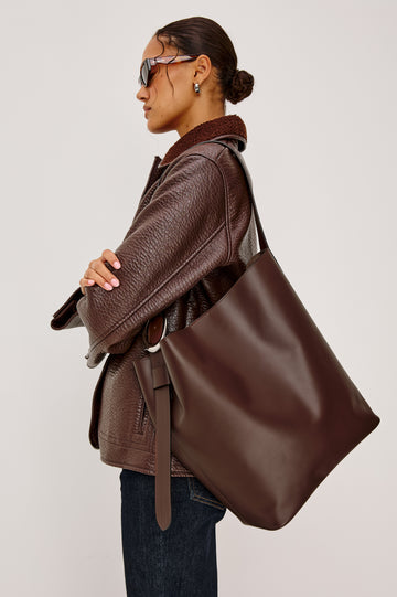 The Torino is a soft leather bucket bag, designed with an adjustable strap and polished silver oval buckle, in espresso colorway. Side view featured on model.