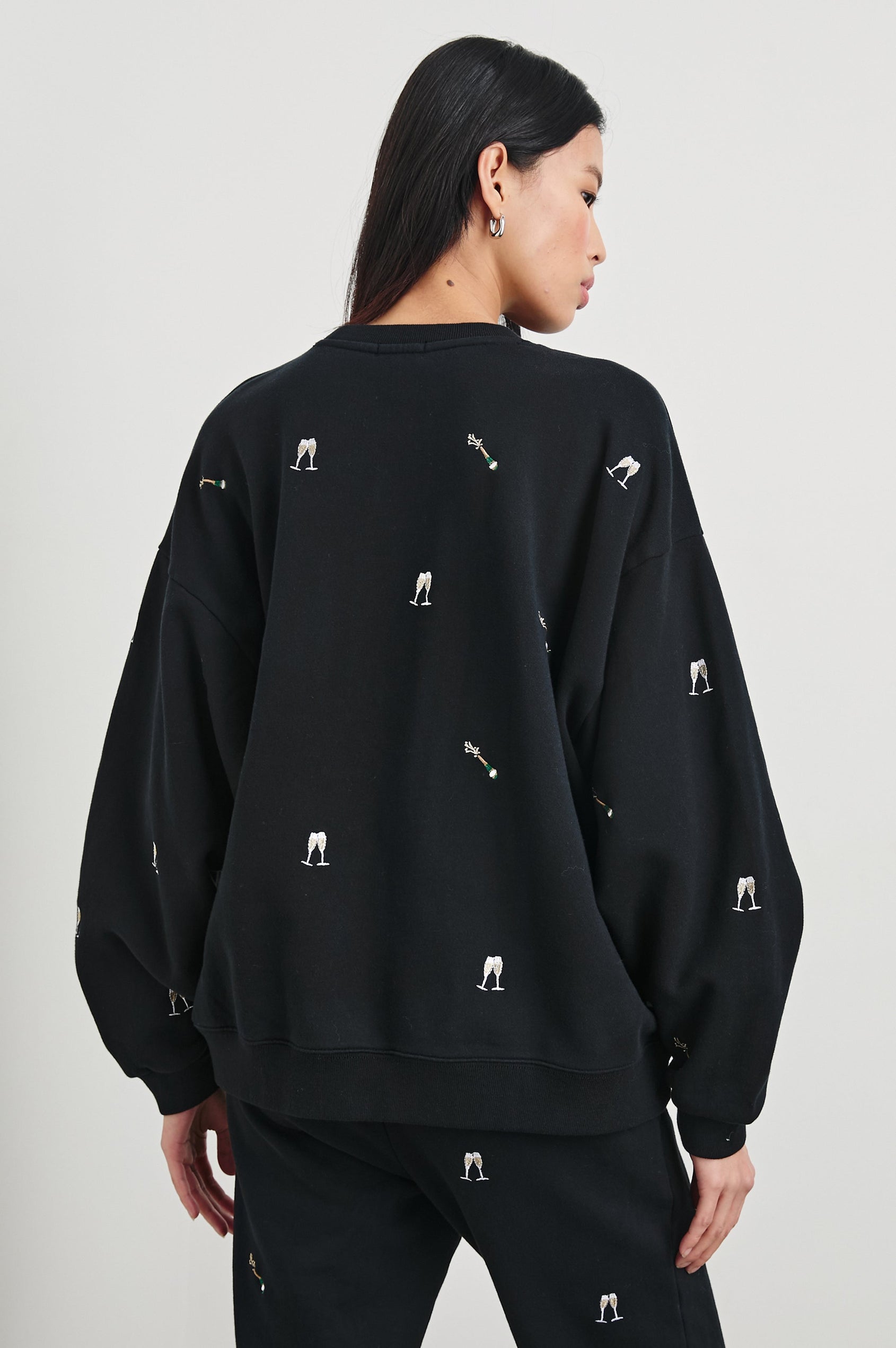 The Varsity Sweatshirt with a Crew Neck and embroidered Champagne Glasses in Black Champagne Embroidery Colorway, on Black - Back View Featured on Model 