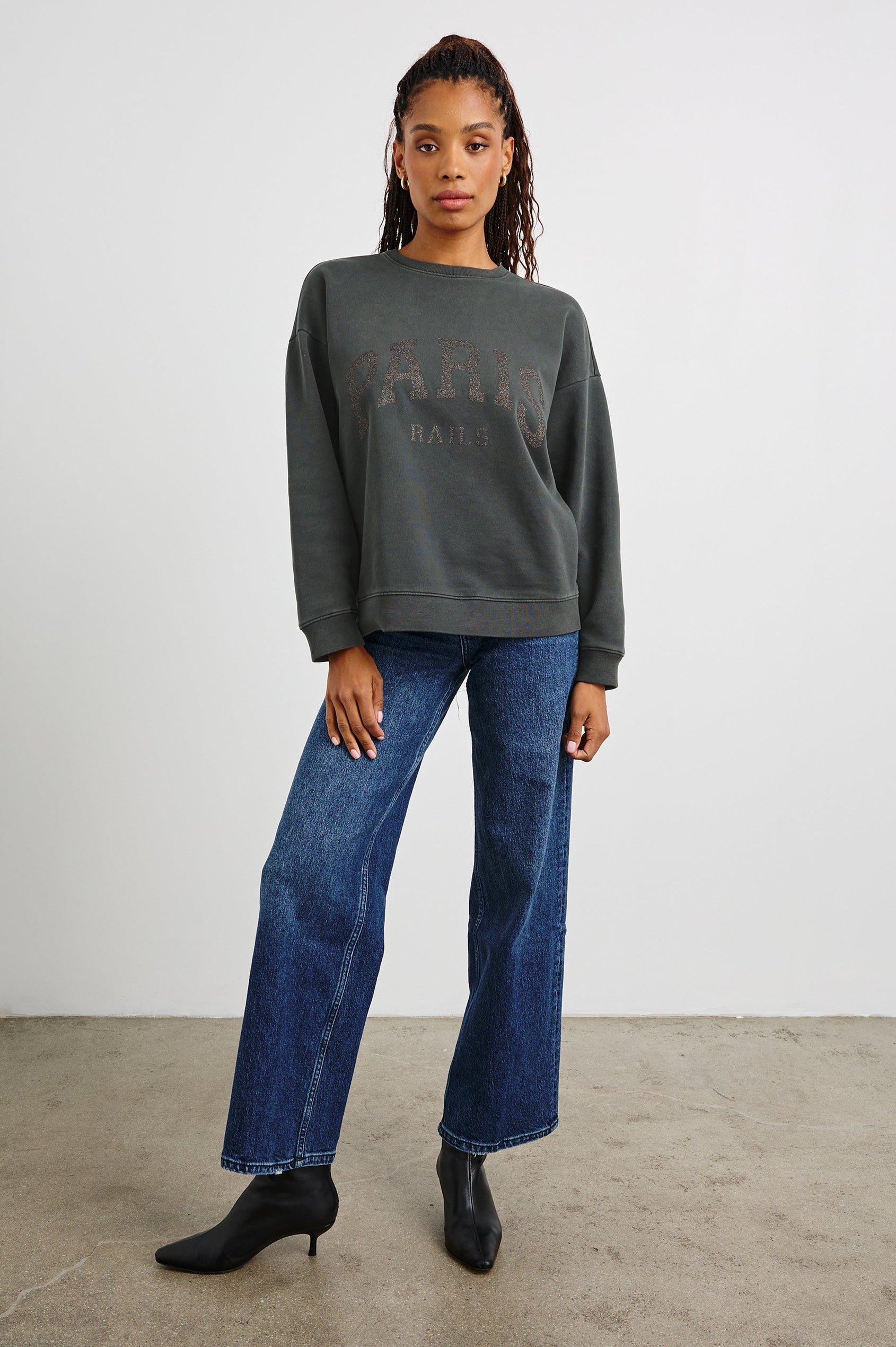 The Varsity Sweatshirt with a Crew Neck and Glitter Text states, Paris Rails in Paris Glitter Colorway, on dark grey - Front Full Body View Featured on Model 