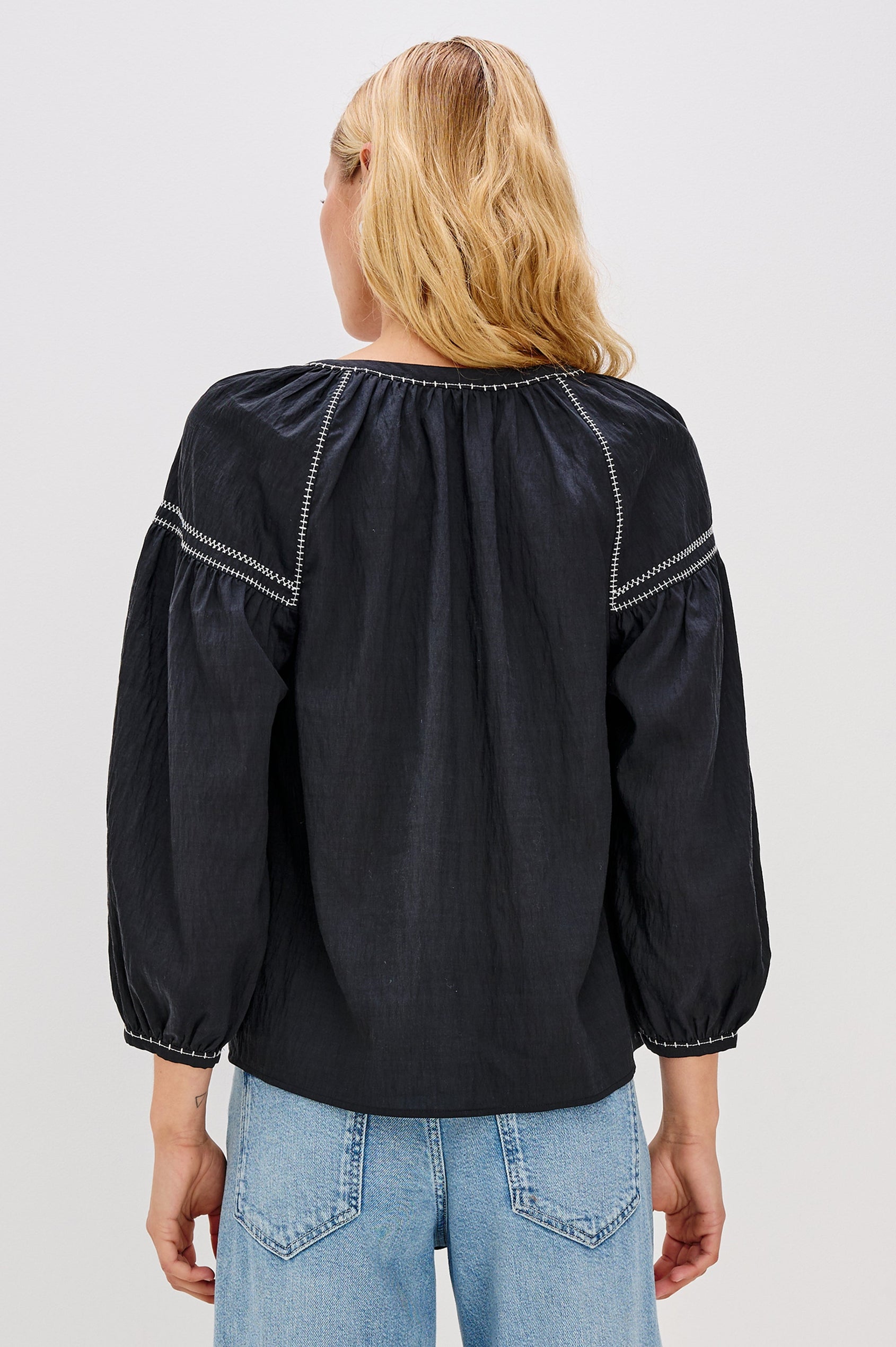 The Vasia is a long sleeve peasant top with a v-neck and button front, contrast white stitching and elastic at sleeve hems in Black colorway. Back view featured on model.