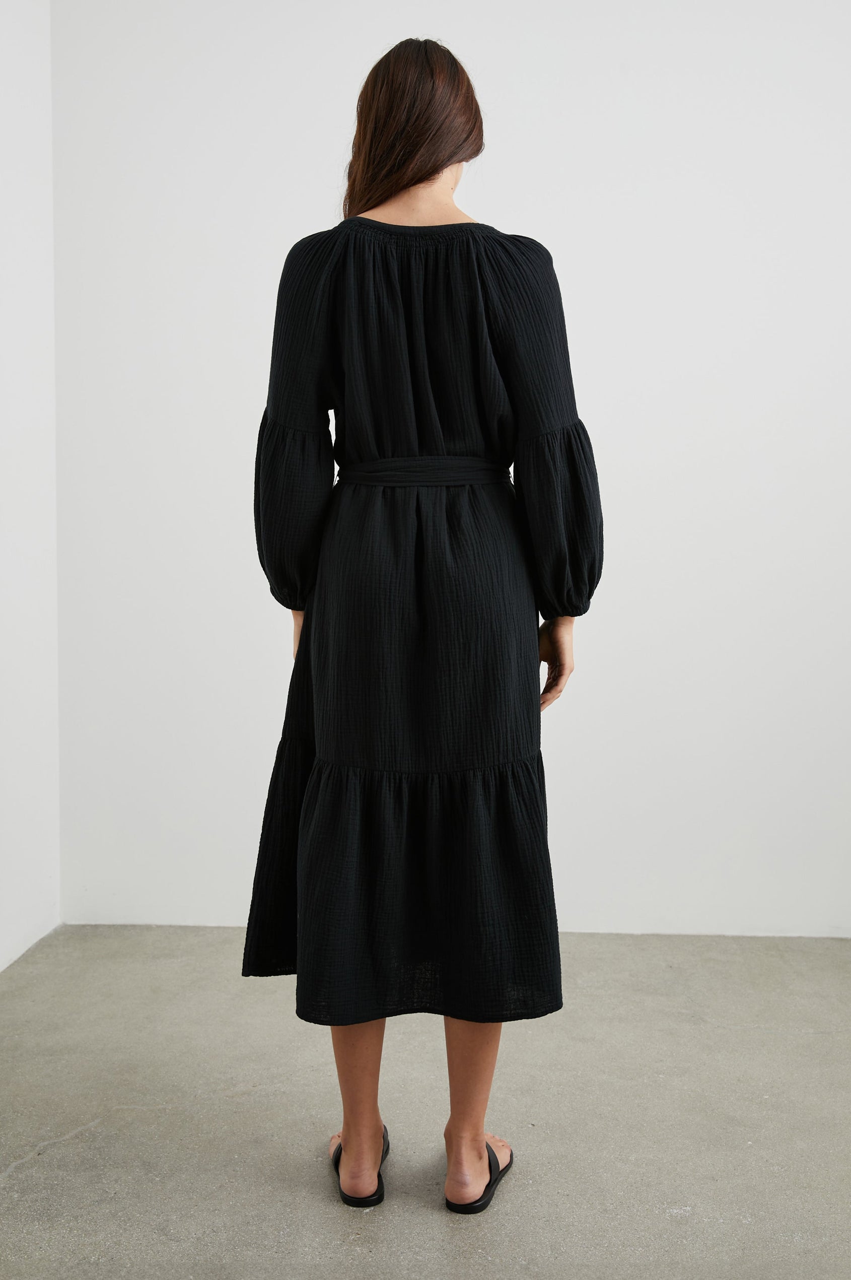 Vittoria Midi Dress with Three-Quarter Sleeves, a V Neck, Light Ruching at the Collar, and a Fabric Tie Belt in Black Colorway - Back Full Body View Featured on Model