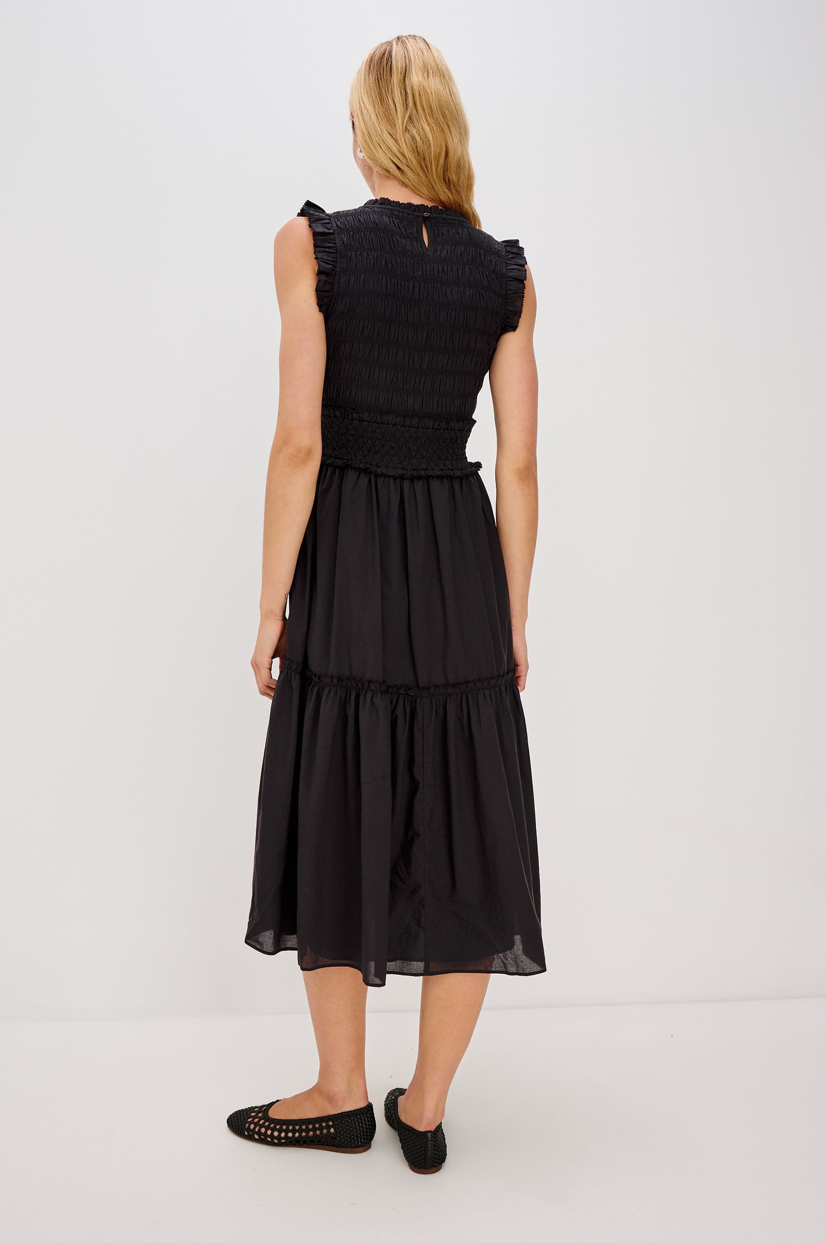 Vivier is a crinkled cotton poplin maxi dress featuring a smocked, fitted bodice and waistband. The dress flows into a relaxed skirt with soft ruffled tiers, creating a breezy silhouette in Black Colorway - Back View Featured on Model