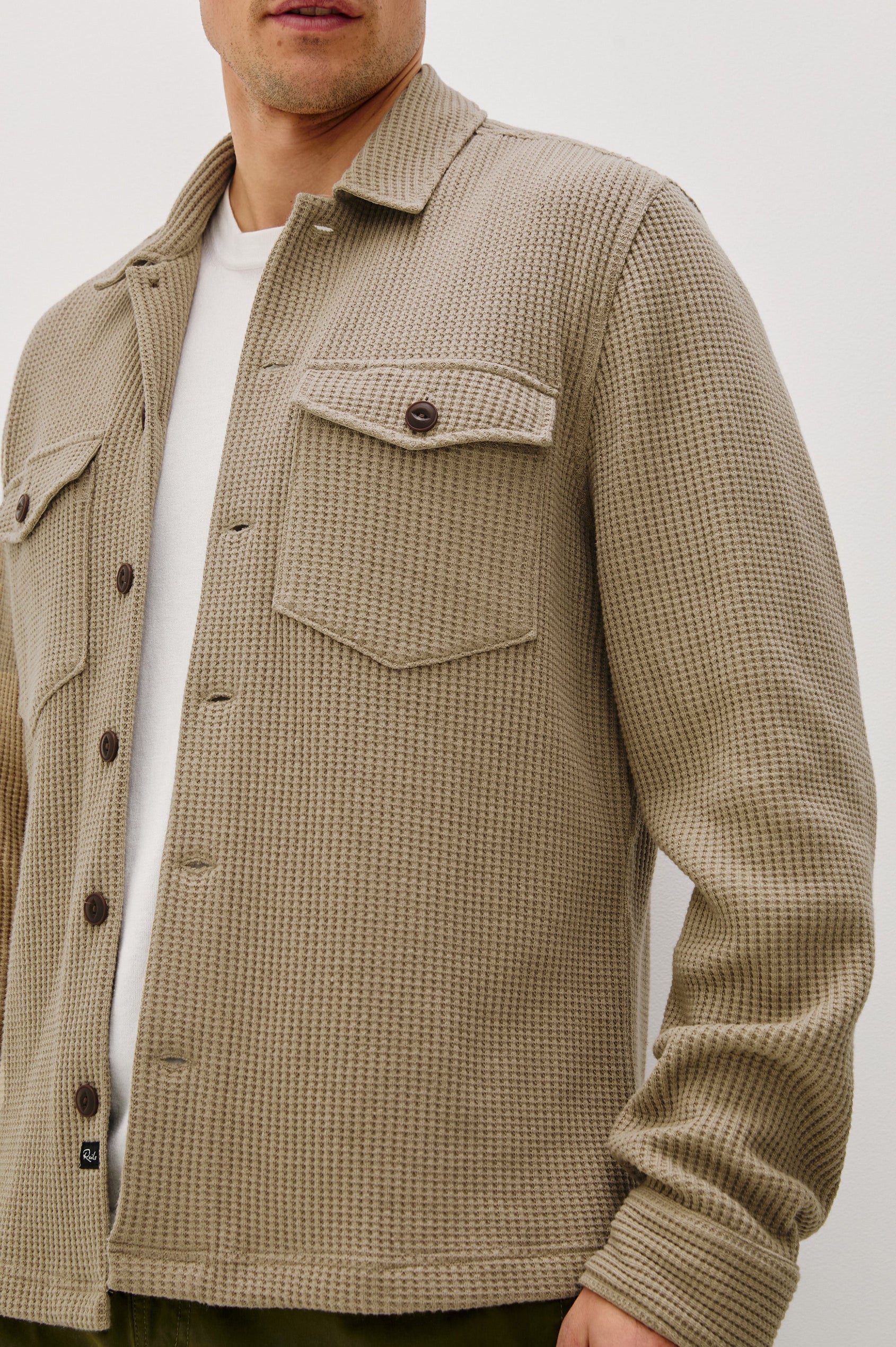 The Wells is a collared button front shirt jacket with contrast brown buttons and two chest pockets in Barley colorway. Front detail view featured on model.