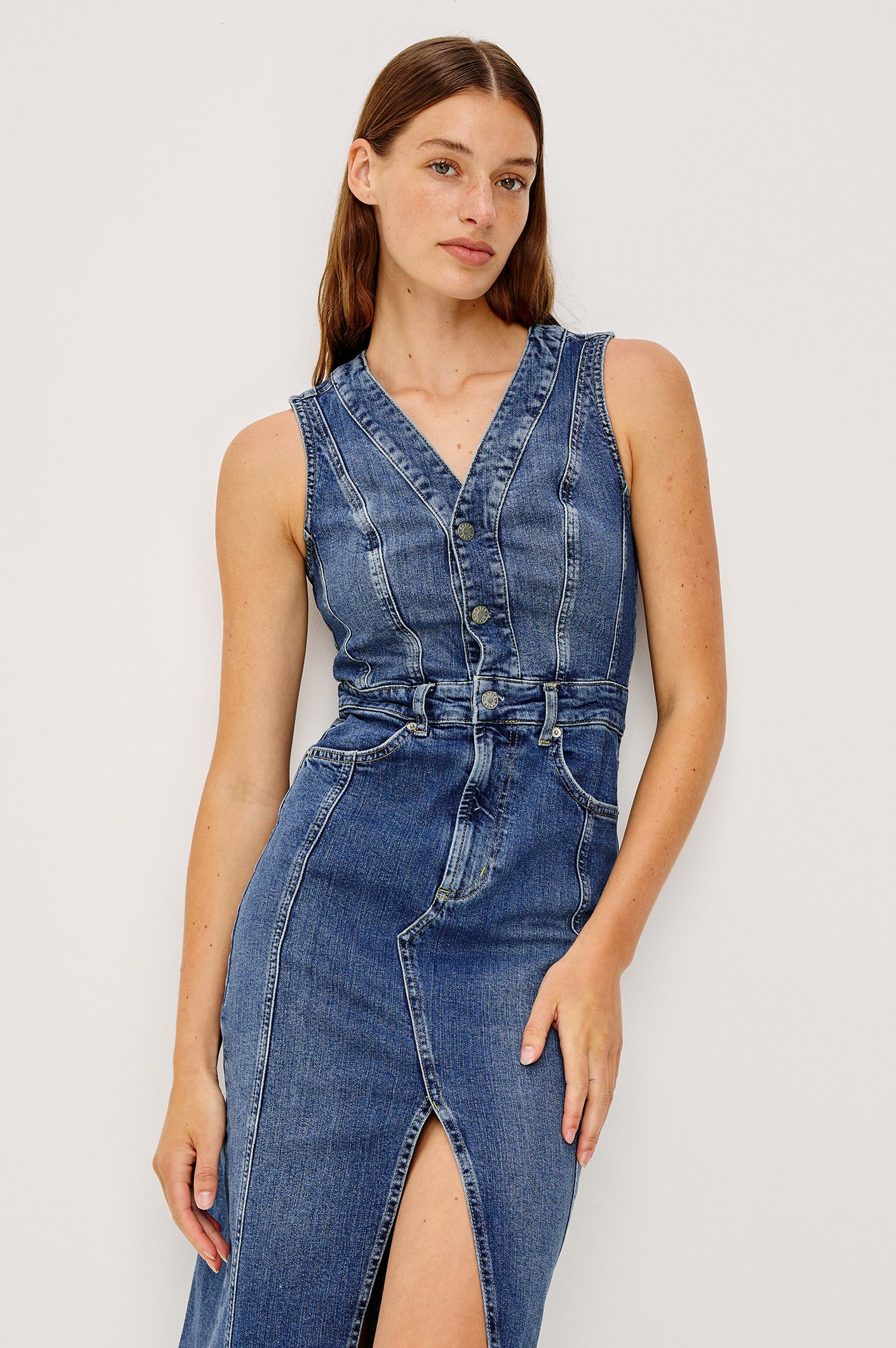 Westwood Sleeveless Denim Midi Dress with Belt Loops, a Button and Zipper Closure for the Skirt and Button Closure on the Bodice, a V neck, a Front Center Thigh Slit, Two Front Pockets  and Two Back Patch Pockets in Forget Me Not Colorway, a Blue - Close Up Front View Featured on Model